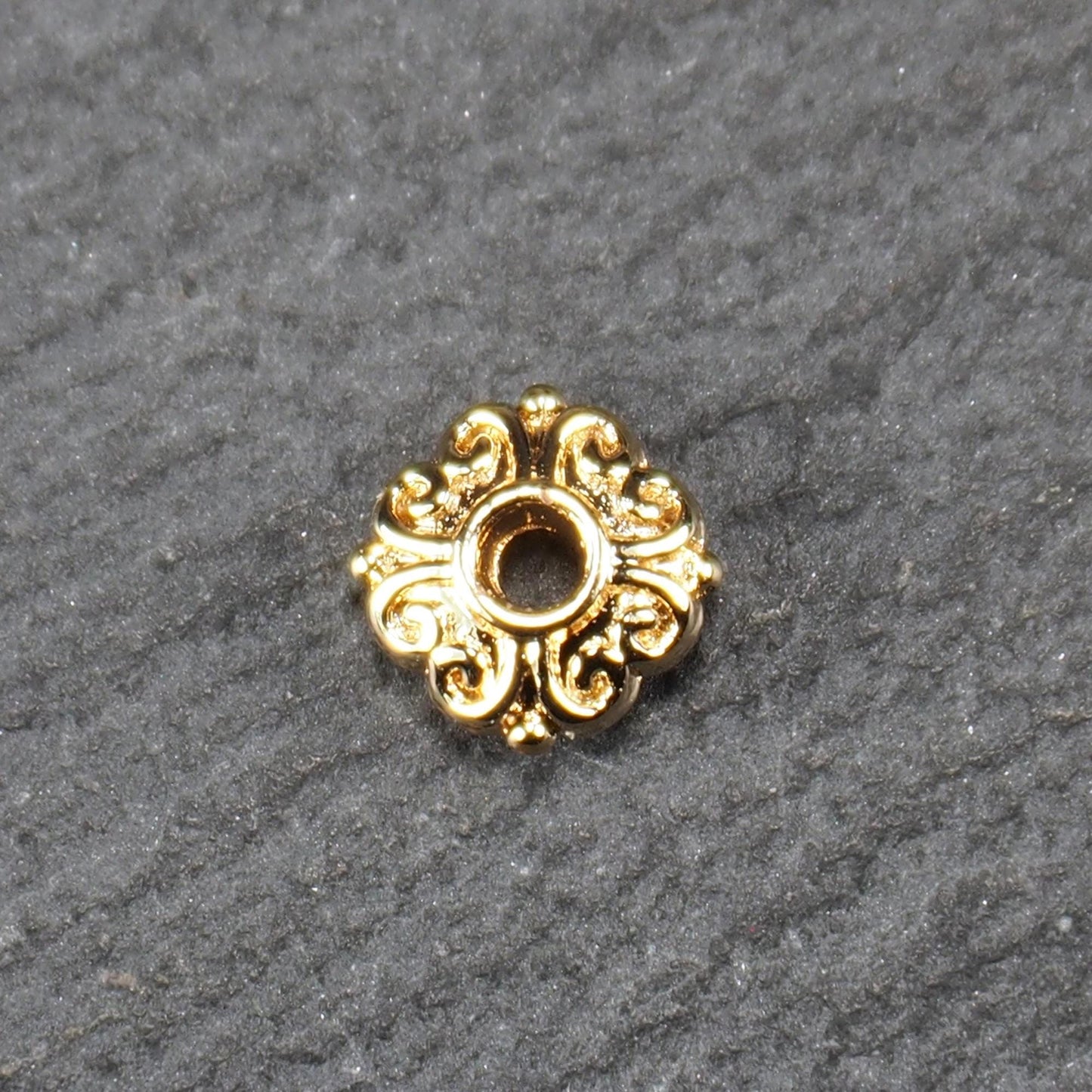Runde goldfarbene Spacer Perle mit glänzender Oberfläche, reliefartigem floralem Ornament und zentralem runden Durchbruch.