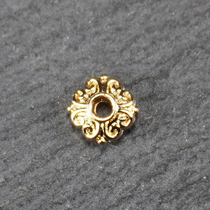 Runde goldfarbene Spacer Perle mit glänzender Oberfläche, reliefartigem floralem Ornament und zentralem runden Durchbruch.
