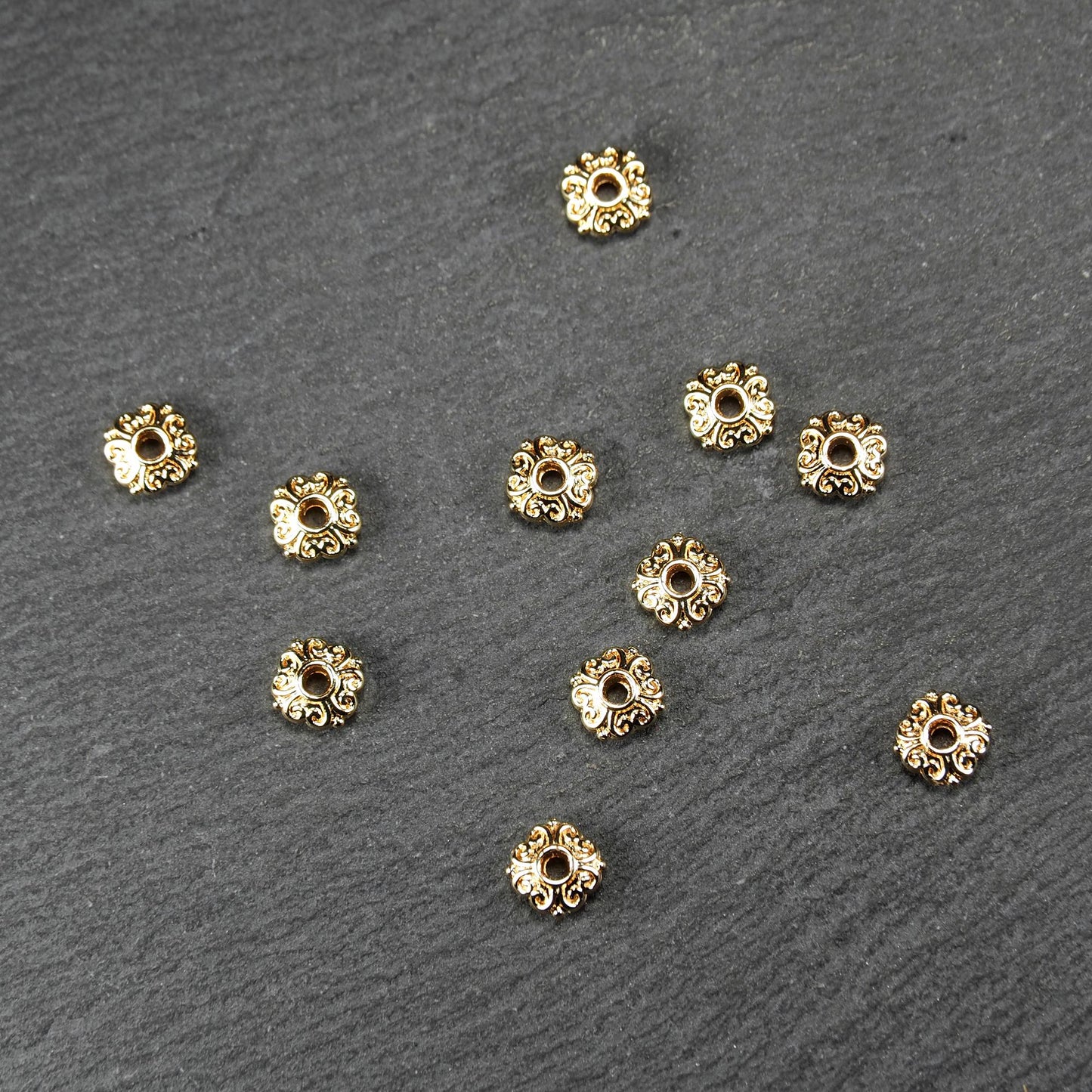Runde goldfarbene Spacer Perlen mit glänzender Oberfläche, reliefartigem floralem Ornament und zentralem runden Durchbruch.