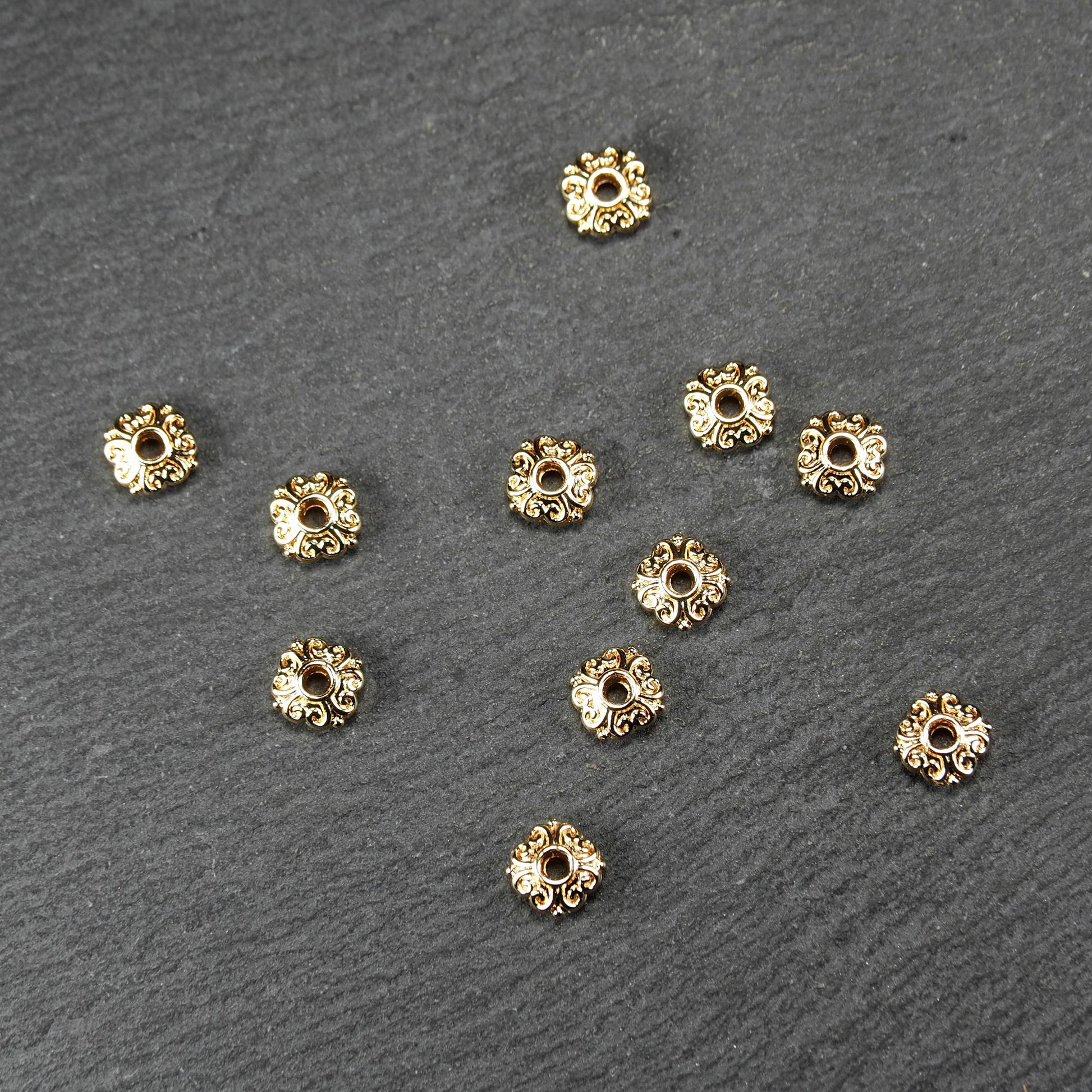 Runde goldfarbene Spacer Perlen mit glänzender Oberfläche, reliefartigem floralem Ornament und zentralem runden Durchbruch.