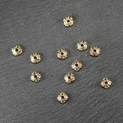 Runde goldfarbene Spacer Perlen mit glänzender Oberfläche, reliefartigem floralem Ornament und zentralem runden Durchbruch.