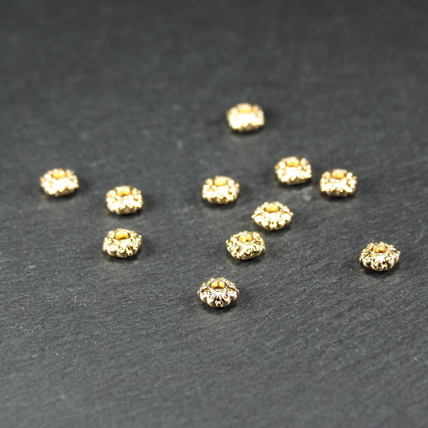 Runde goldfarbene Spacer Perlen mit glänzender Oberfläche, reliefartigem floralem Ornament und zentralem runden Durchbruch.