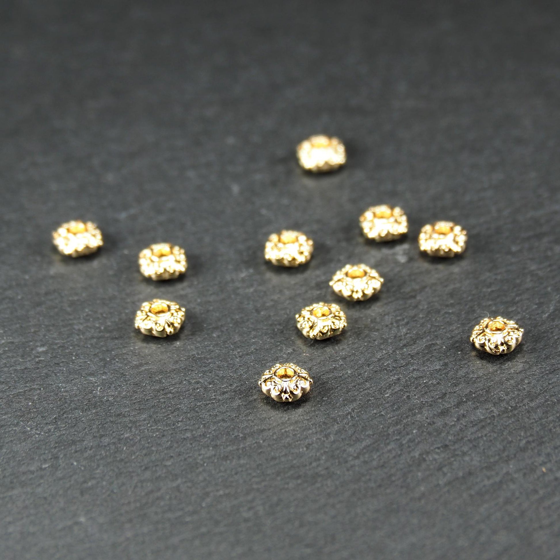 Runde goldfarbene Spacer Perlen mit glänzender Oberfläche, reliefartigem floralem Ornament und zentralem runden Durchbruch.