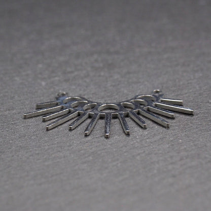 Versilberter Metallverbinder, halbkreisförmig und durchbrochen, mit rundem Mittelloch, mehreren schmalen radialen Strahlen, glänzender Oberfläche und zwei kleinen Ösen oben.