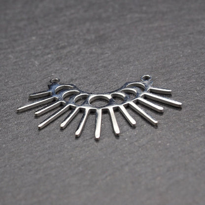 Versilberter Metallverbinder, halbkreisförmig und durchbrochen, mit rundem Mittelloch, mehreren schmalen radialen Strahlen, glänzender Oberfläche und zwei kleinen Ösen oben.