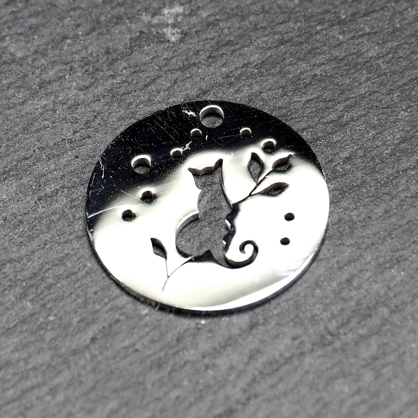 Runder, flacher Anhänger aus poliertem Edelstahl, Cut-out mit sitzender Katzen-Silhouette und Blattzweig, Öse oben und mehrere kleine Bohrungen.
