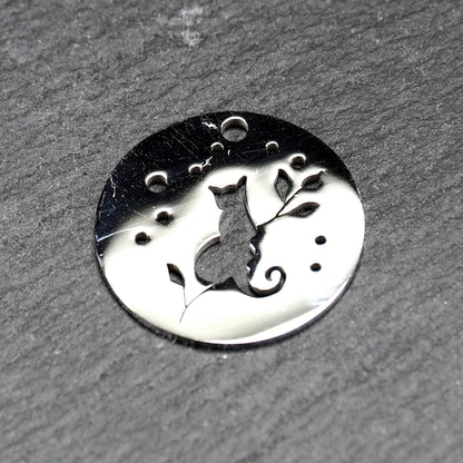 Runder, flacher Anhänger aus poliertem Edelstahl, Cut-out mit sitzender Katzen-Silhouette und Blattzweig, Öse oben und mehrere kleine Bohrungen.