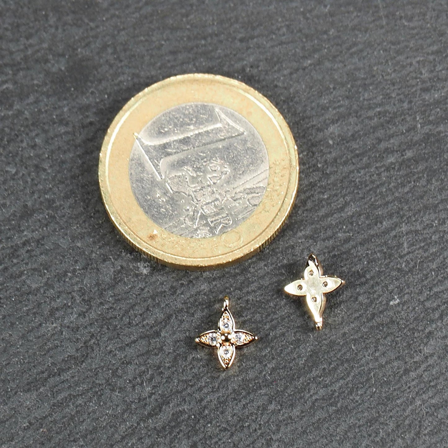 Vierblättriger goldfarbener Anhänger mit vier eingelassenen klaren Steinchen und zentraler Kugel, Öse sichtbar; daneben 1‑Euro‑Münze.