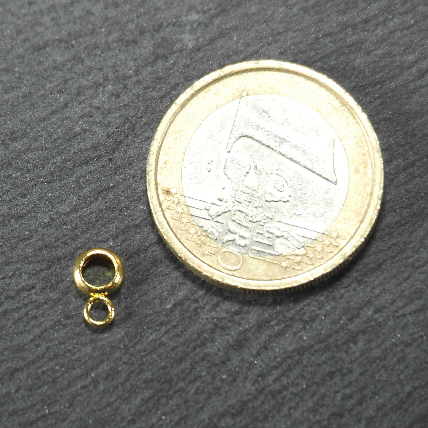 Anhängeröse, goldfarben und glänzend, ringförmig mit zusätzlicher kleiner Öse, neben einer 1‑Euro‑Münze zur Größendarstellung.