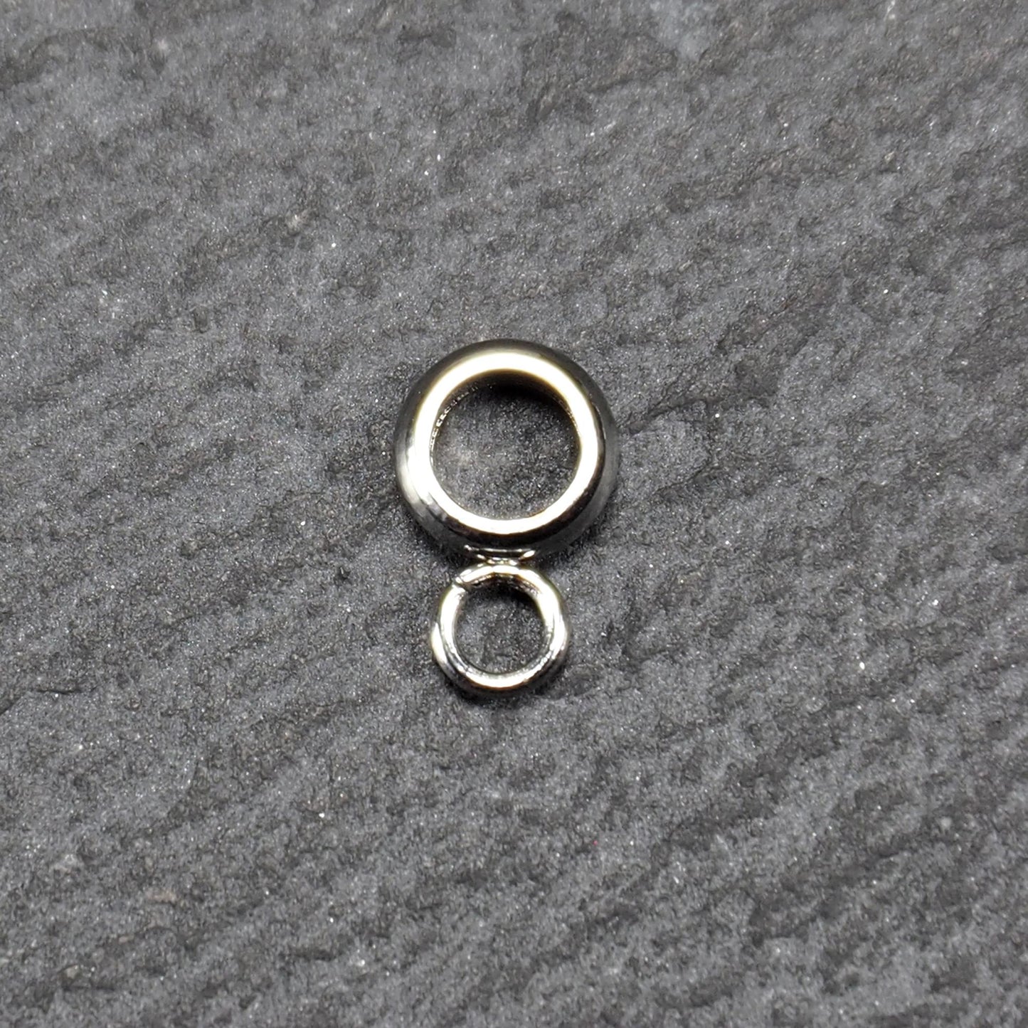 Runde Anhängeröse mit silberglänzender Oberfläche, kompakter durchbrochener Ring mit kleinem geschlossenen Ring unten.