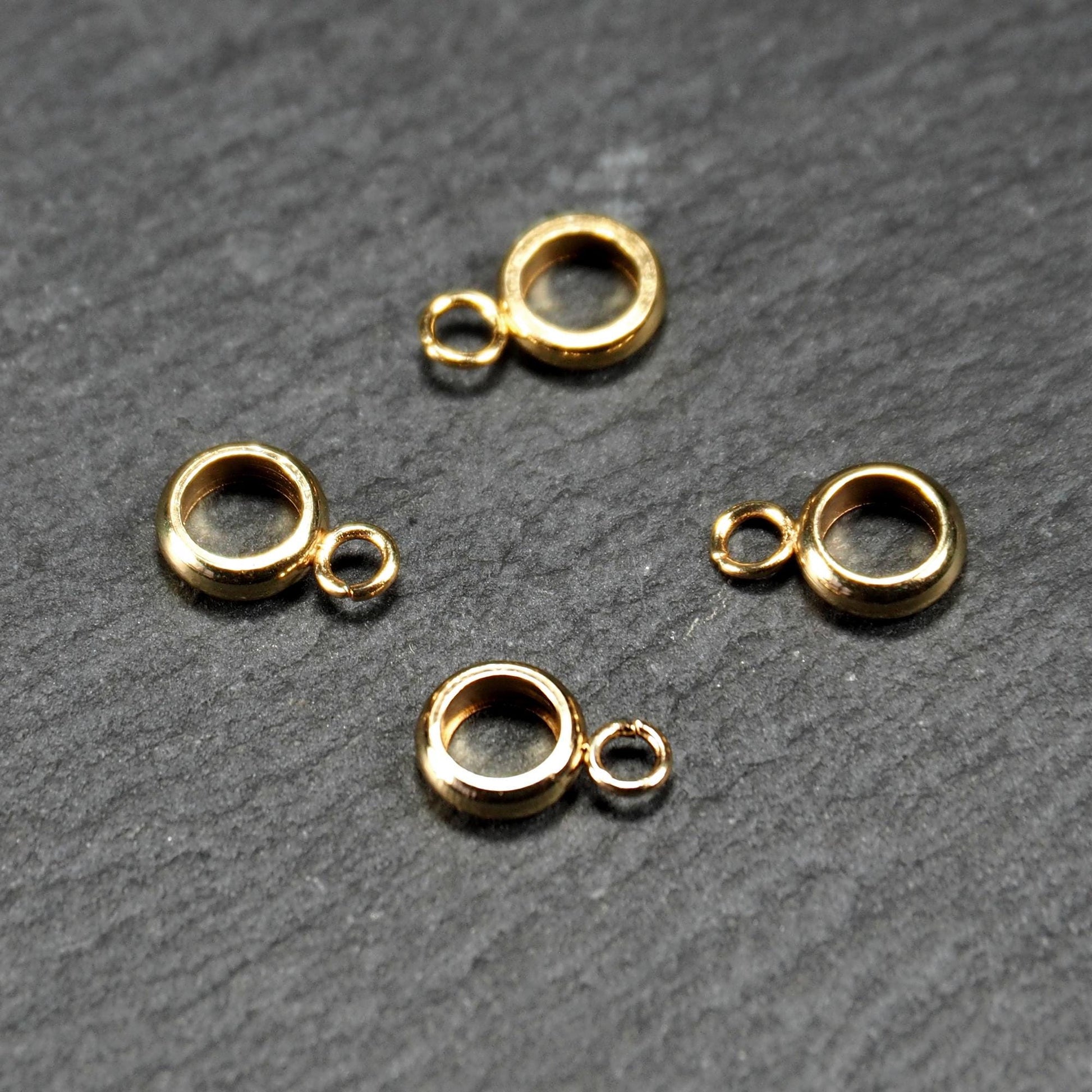 Vier vergoldete ringförmige Anhängerösen mit glänzender goldfarbener Oberfläche, hohlem Mittelring und jeweils kleinem seitlichem Ösenring.