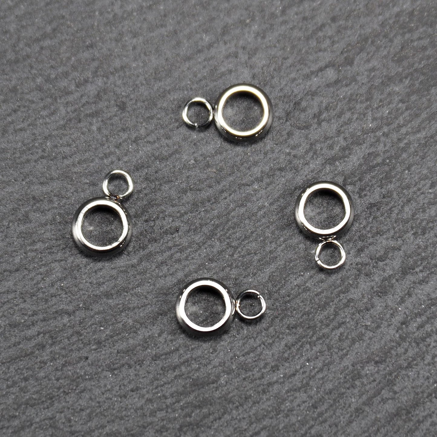 Vier glänzende silberfarbene runde Anhängerösen, jeweils ein größerer hohler Ring mit einer kleineren beweglichen Ringöse.
