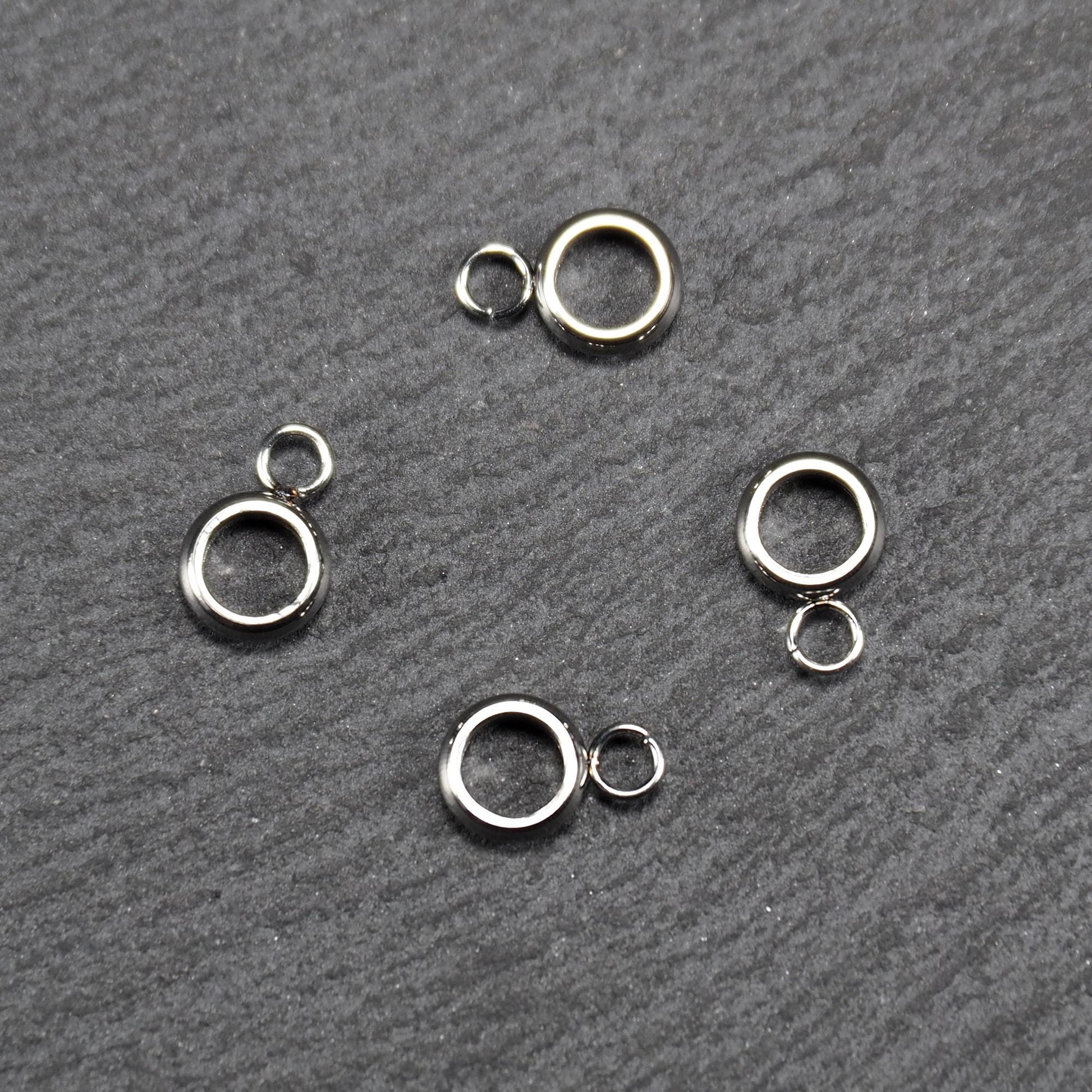 Vier glänzende silberfarbene runde Anhängerösen, jeweils ein größerer hohler Ring mit einer kleineren beweglichen Ringöse.