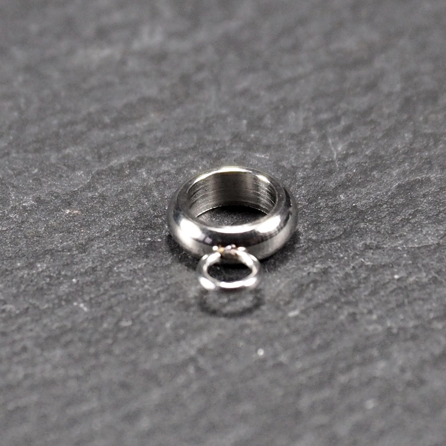 Anhängeröse, silberfarbene glänzende Metallrundung mit zentraler Öffnung und einer kleineren beweglichen Ringöse als Verbindungselement.