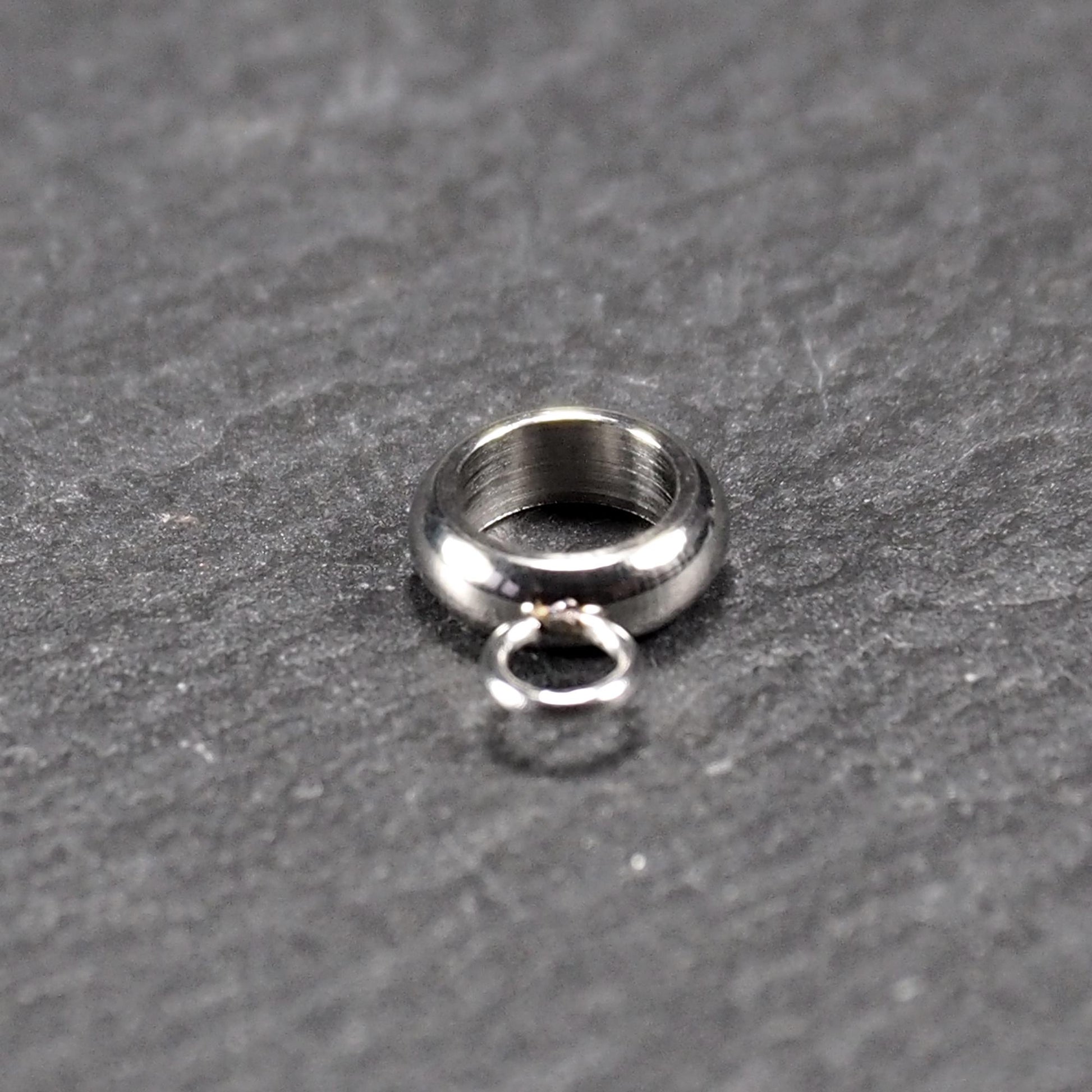 Anhängeröse, silberfarbene glänzende Metallrundung mit zentraler Öffnung und einer kleineren beweglichen Ringöse als Verbindungselement.