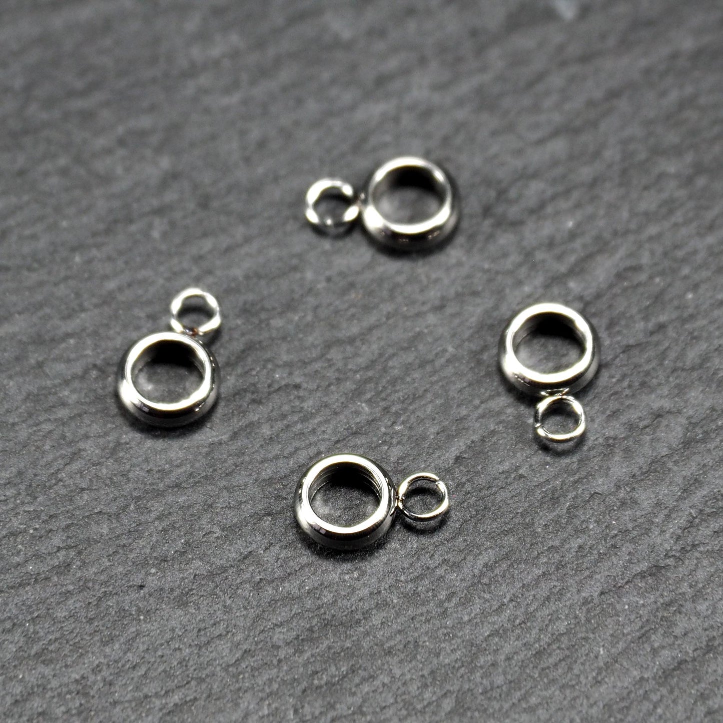 Vier glänzende silberfarbene runde Anhängerösen, jeweils ein größerer hohler Ring mit einer kleineren beweglichen Ringöse.