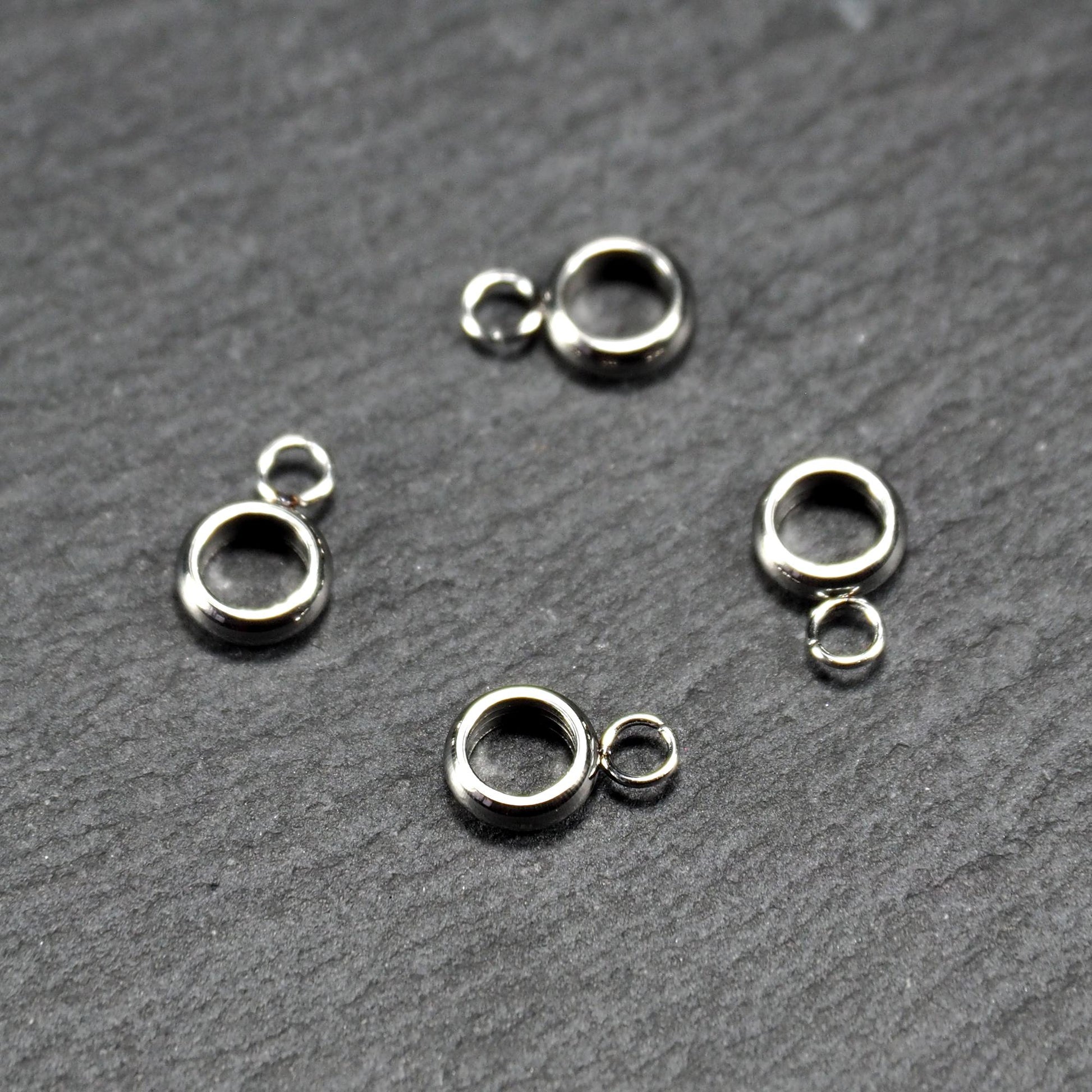 Vier glänzende silberfarbene runde Anhängerösen, jeweils ein größerer hohler Ring mit einer kleineren beweglichen Ringöse.