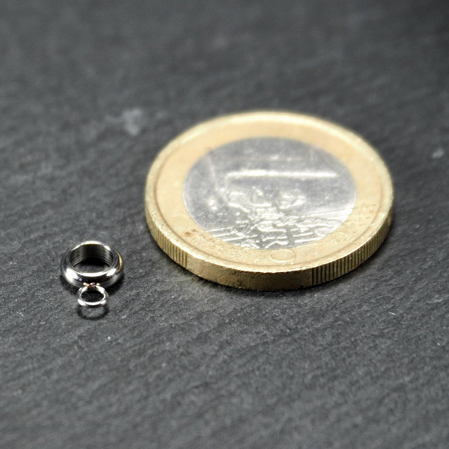 Runde silberfarbene glänzende Anhängeröse mit zusätzlicher kleiner Ringöse, neben einer 1-Euro-Münze zur Größenangabe.