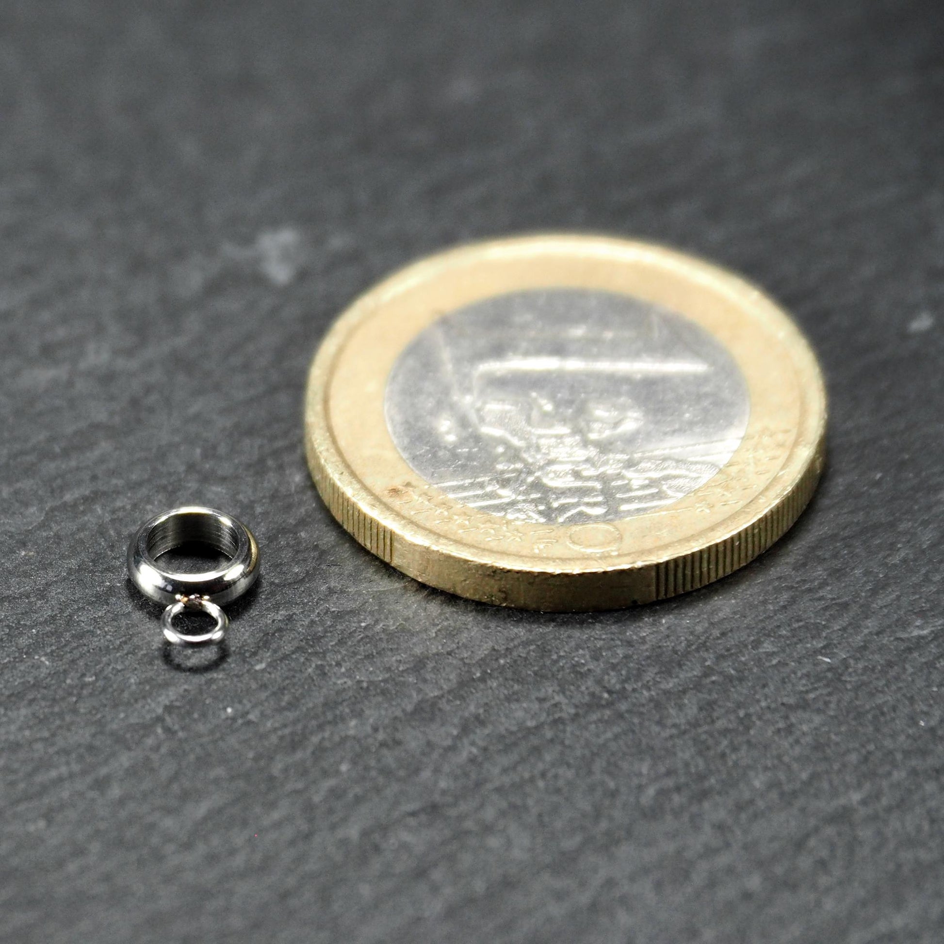 Runde silberfarbene glänzende Anhängeröse mit zusätzlicher kleiner Ringöse, neben einer 1-Euro-Münze zur Größenangabe.