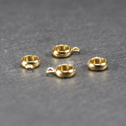 Vier runde, goldfarbene glänzende Anhängerösen in Ringform mit durchbrochenem Innenraum und integrierter kleiner Öse.