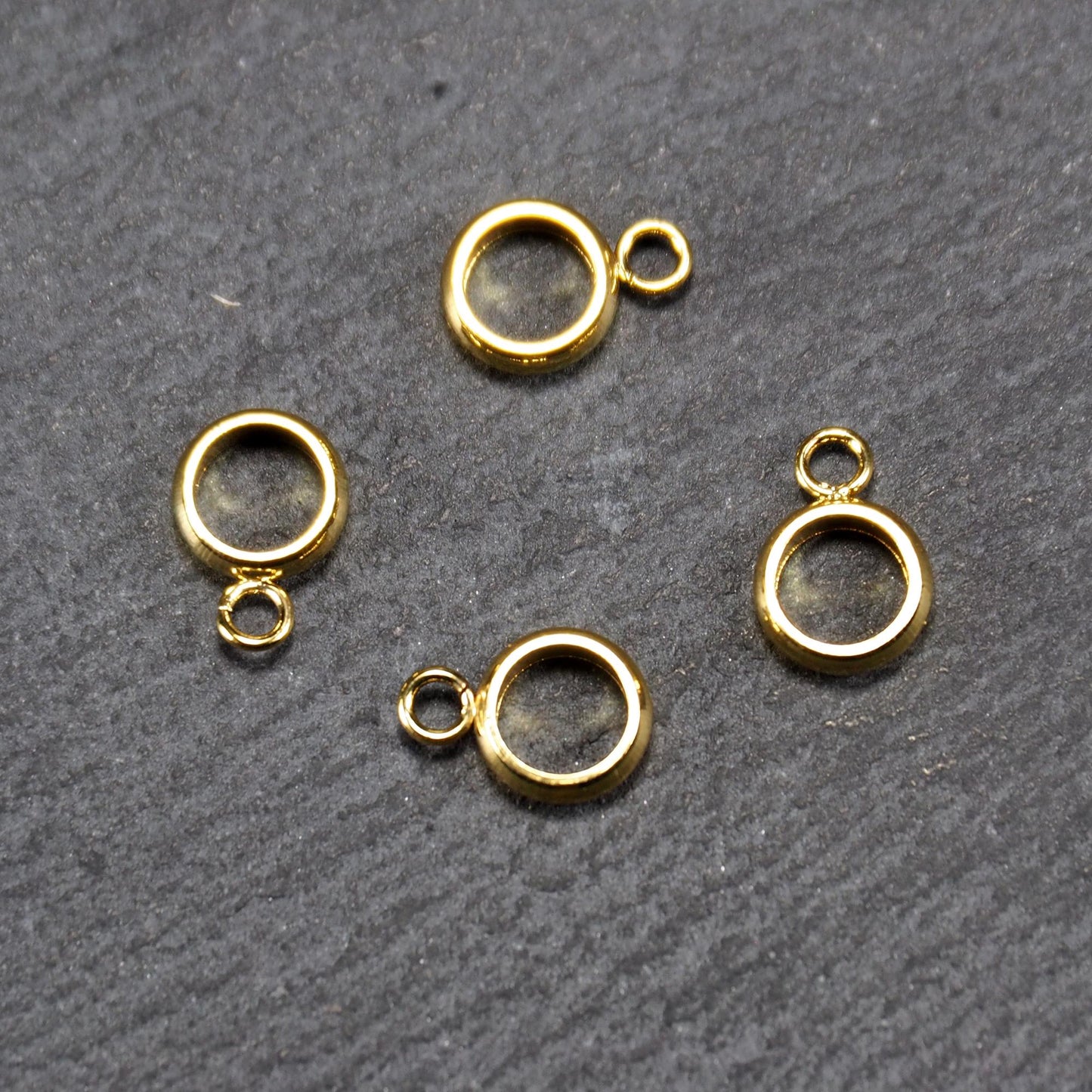 Vier runde, goldfarbene glänzende Anhängerösen in Ringform mit durchbrochenem Innenraum und integrierter kleiner Öse.