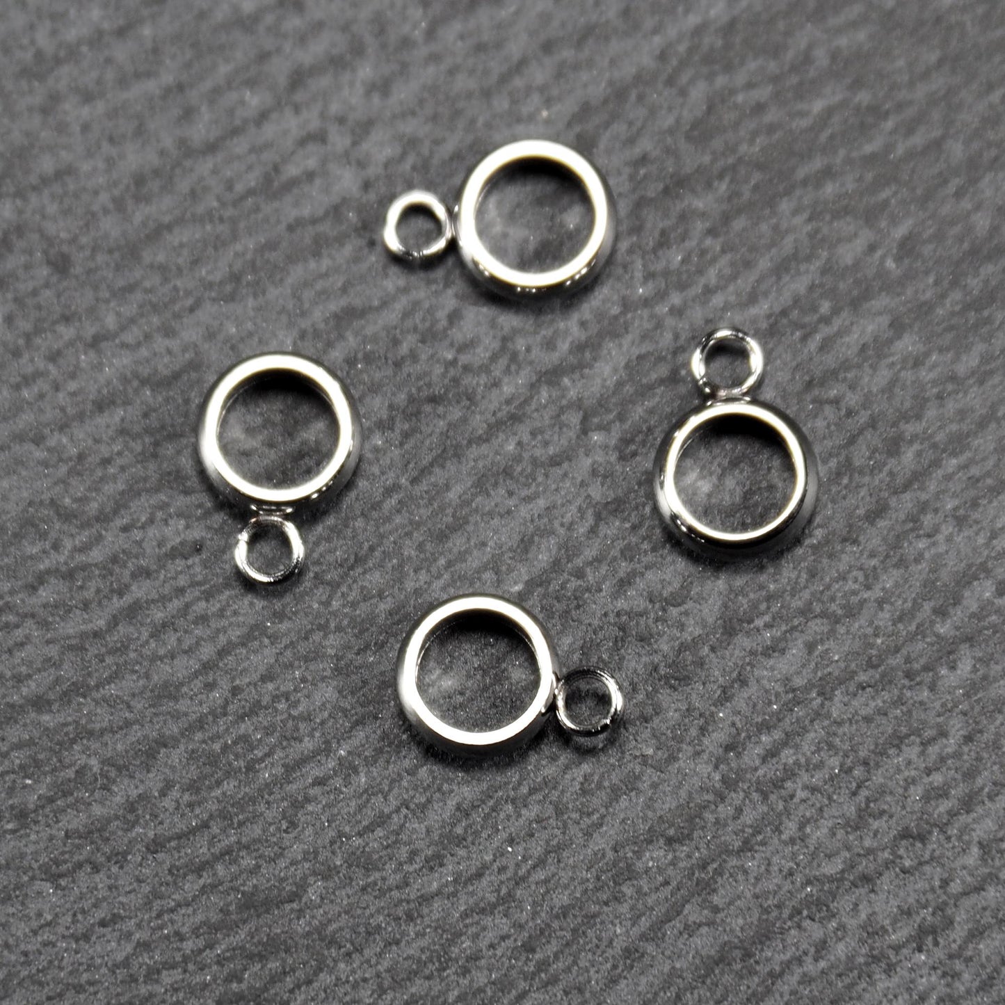Vier runde, silberfarbene Anhängerösen mit glänzender Oberfläche: hohle Ringscheiben mit jeweils einer kleinen Öse.
