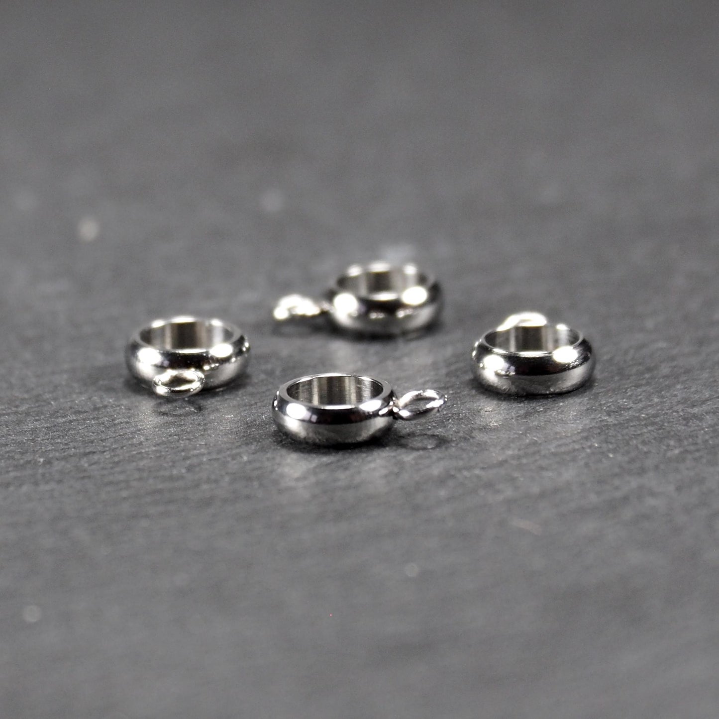 Vier runde, silberfarbene Anhängerösen mit glänzender Oberfläche: hohle Ringscheiben mit jeweils einer kleinen Öse.
