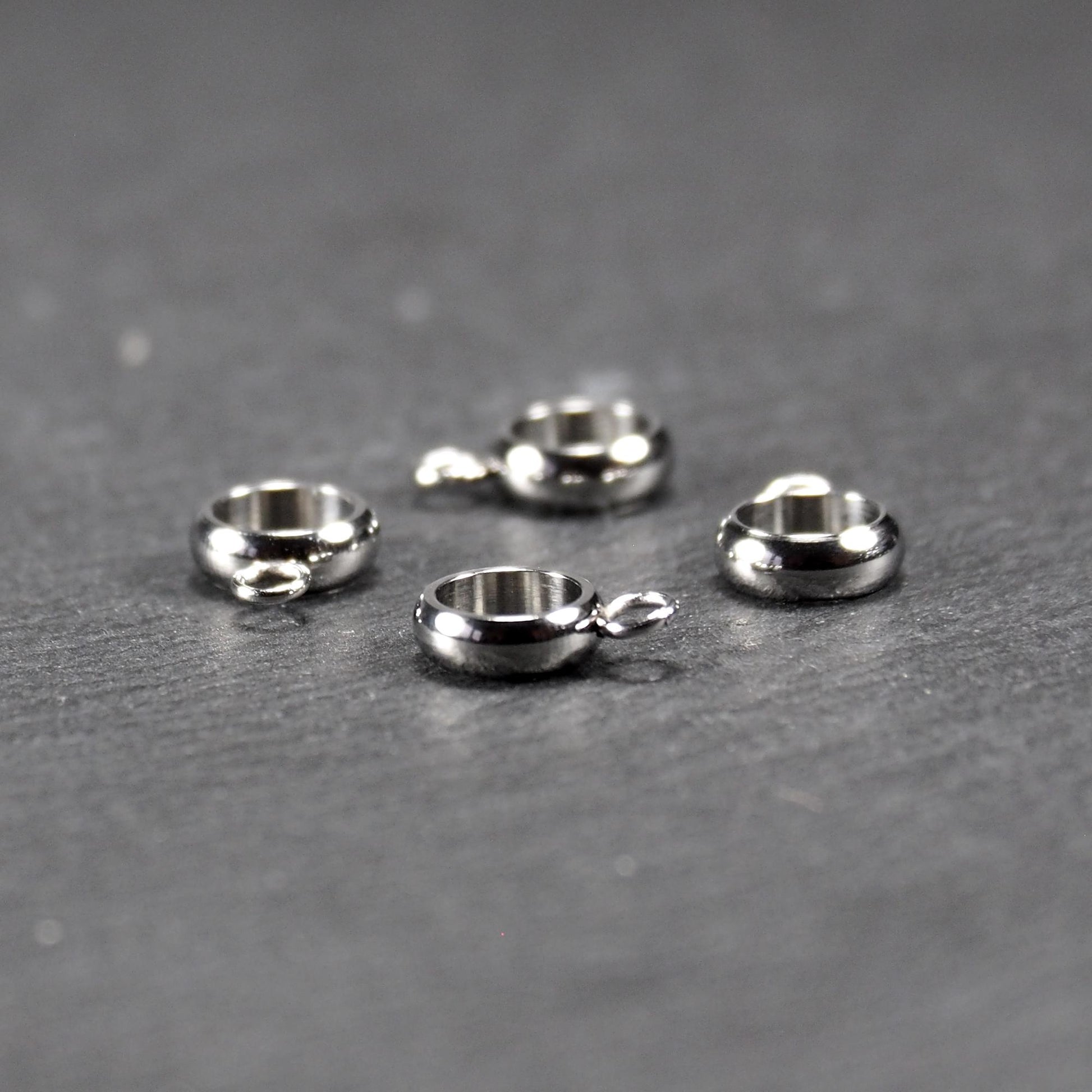 Vier runde, silberfarbene Anhängerösen mit glänzender Oberfläche: hohle Ringscheiben mit jeweils einer kleinen Öse.