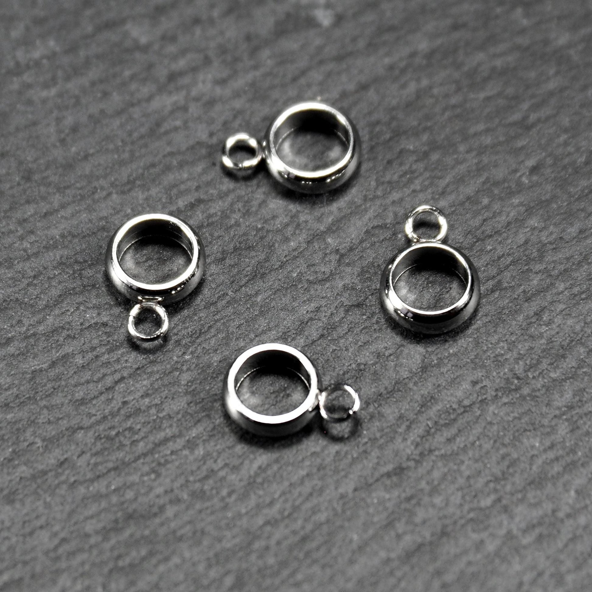 Vier runde, silberfarbene Anhängerösen mit glänzender Oberfläche: hohle Ringscheiben mit jeweils einer kleinen Öse.