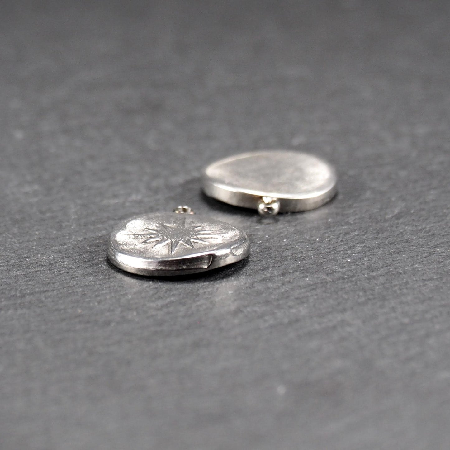 Runder silberner Metallanhänger mit glänzend strukturierter Oberfläche, reliefiertes strahlenförmiges Sonnen-/Kompassmotiv vorn und kleiner Öse oben.