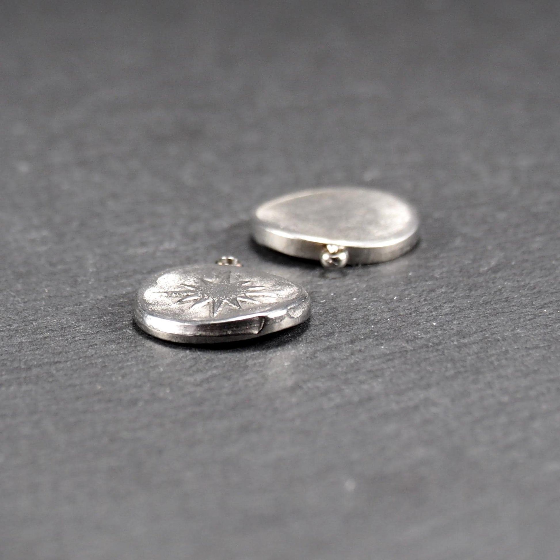 Runder silberner Metallanhänger mit glänzend strukturierter Oberfläche, reliefiertes strahlenförmiges Sonnen-/Kompassmotiv vorn und kleiner Öse oben.