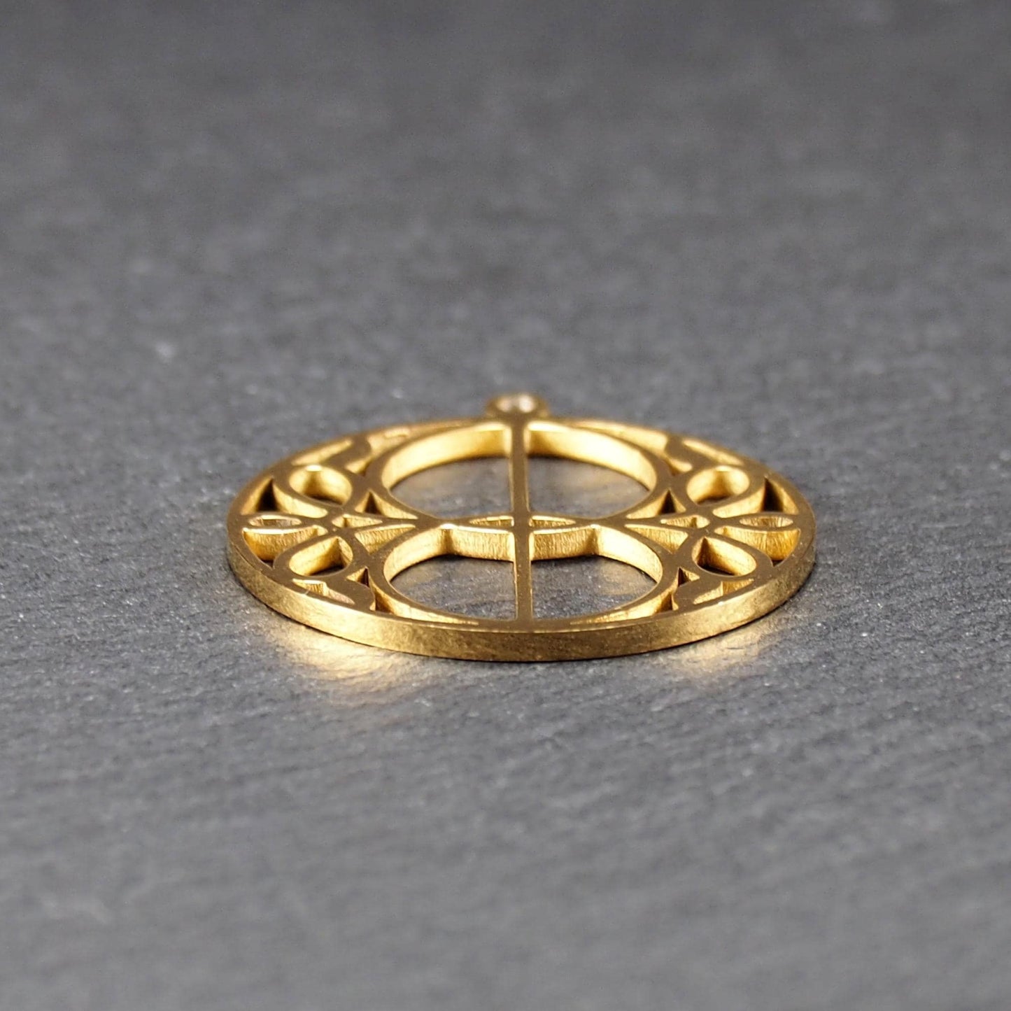 Runder, goldfarbener, filigran durchbrochener Anhänger mit symmetrischem Vesica-Piscis-Ornament und kleiner Öse oben.