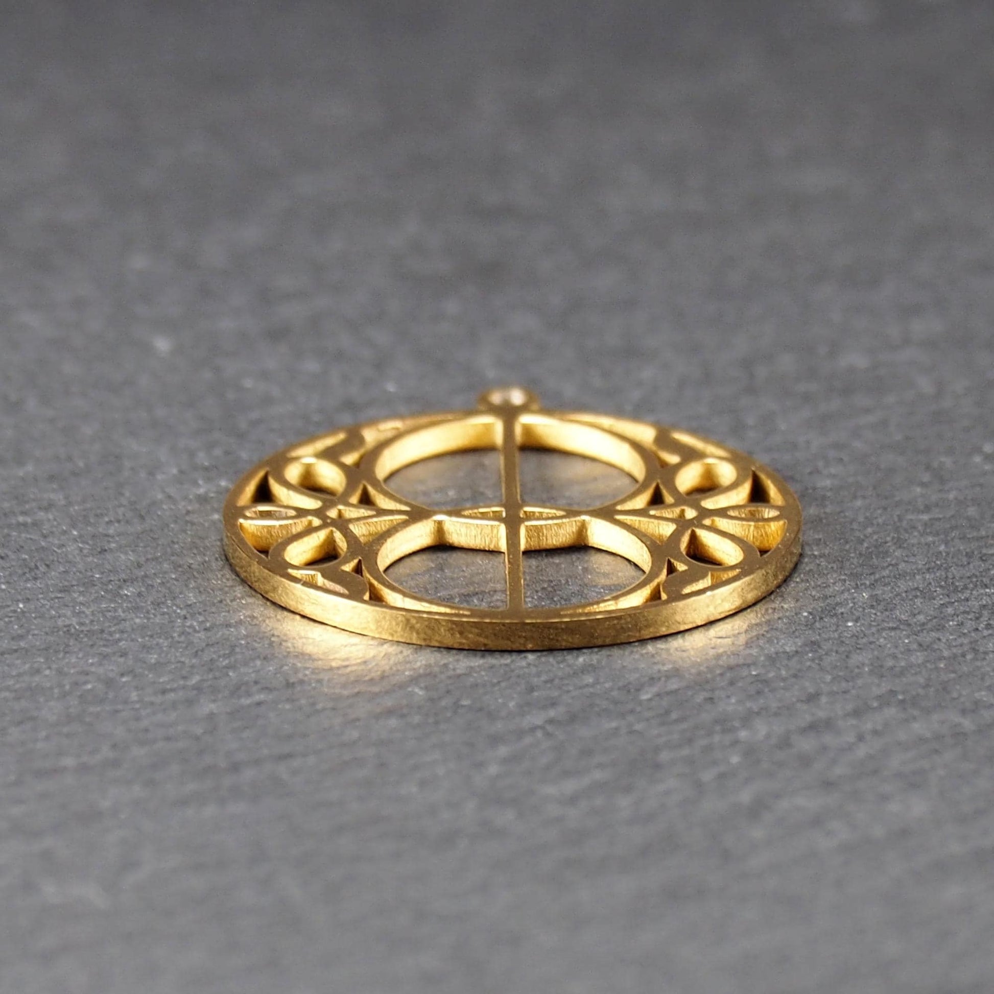 Runder, goldfarbener, filigran durchbrochener Anhänger mit symmetrischem Vesica-Piscis-Ornament und kleiner Öse oben.