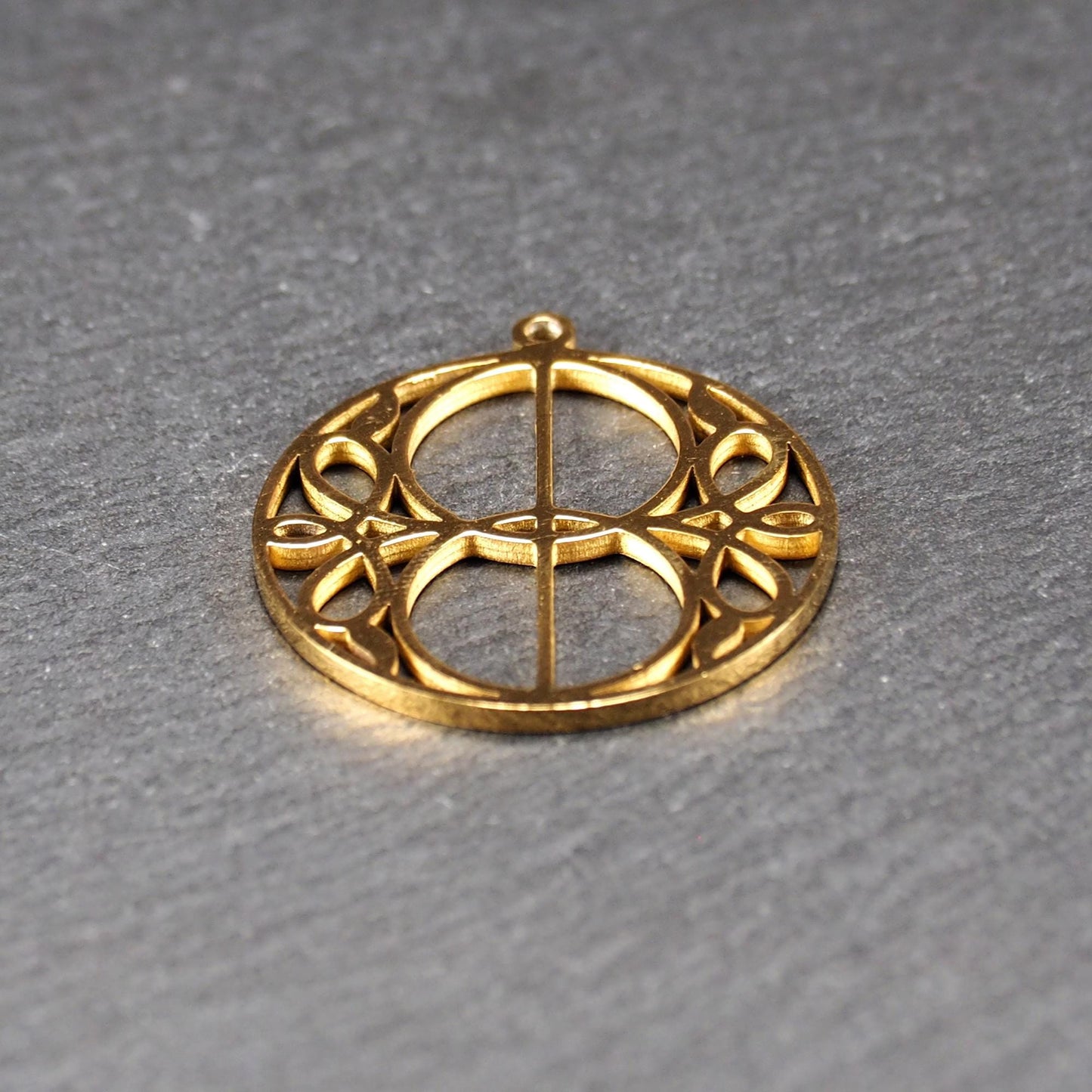 Runder, goldfarbener, filigran durchbrochener Anhänger mit symmetrischem Vesica-Piscis-Ornament und kleiner Öse oben.