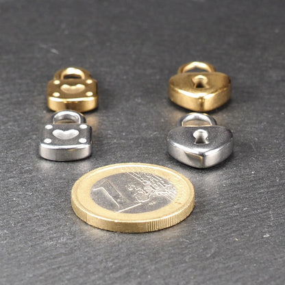 Vier kleine Anhänger in Gold- und Silberton, Schloss- und Schlüsselformen mit Herzmotiv auf glänzender Oberfläche, 1-Euro-Münze als Größenvergleich.