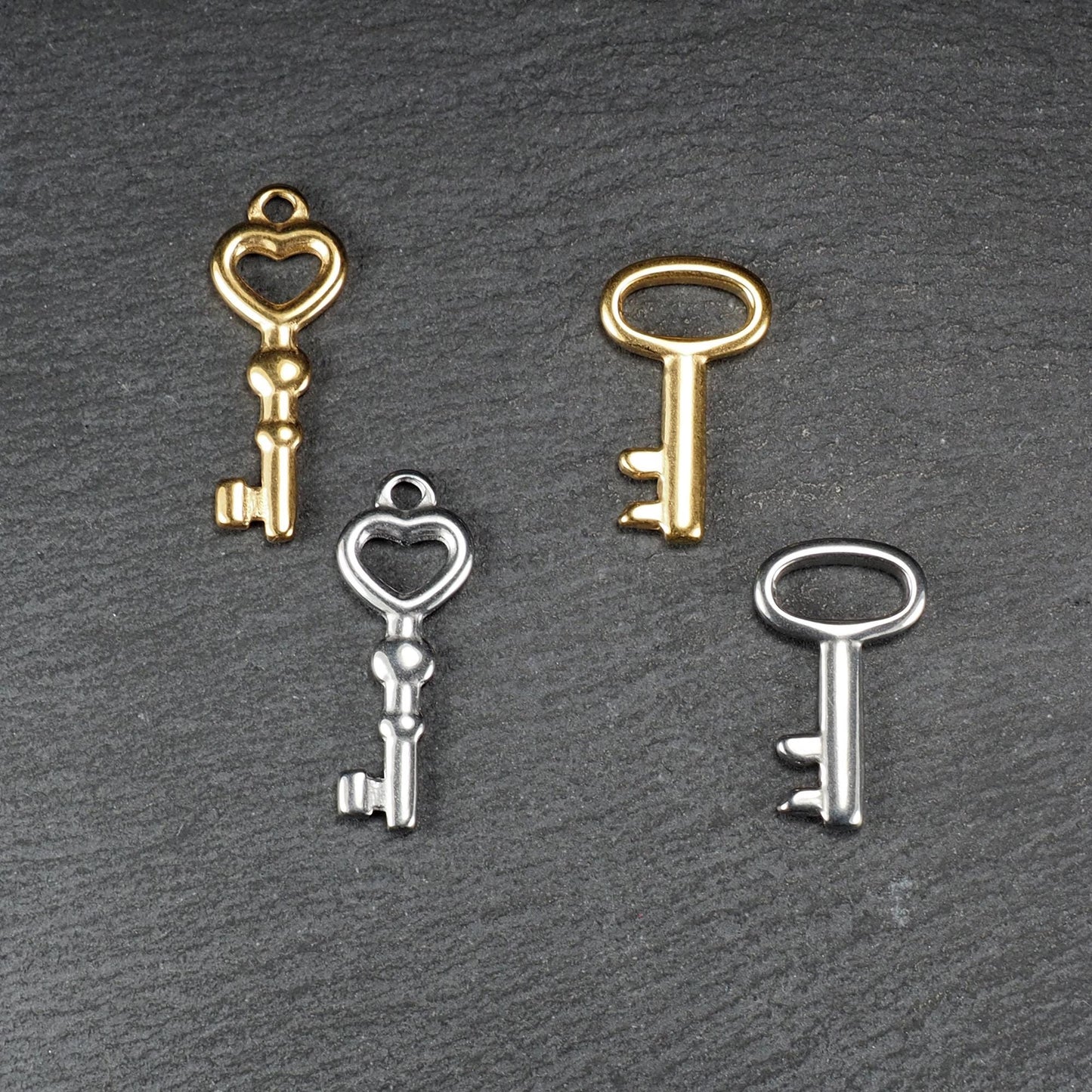 Vier glänzende Schlüsselanhänger, zwei vergoldet und zwei silberfarben; zwei mit herzförmiger Öse, zwei mit ovaler Öse.