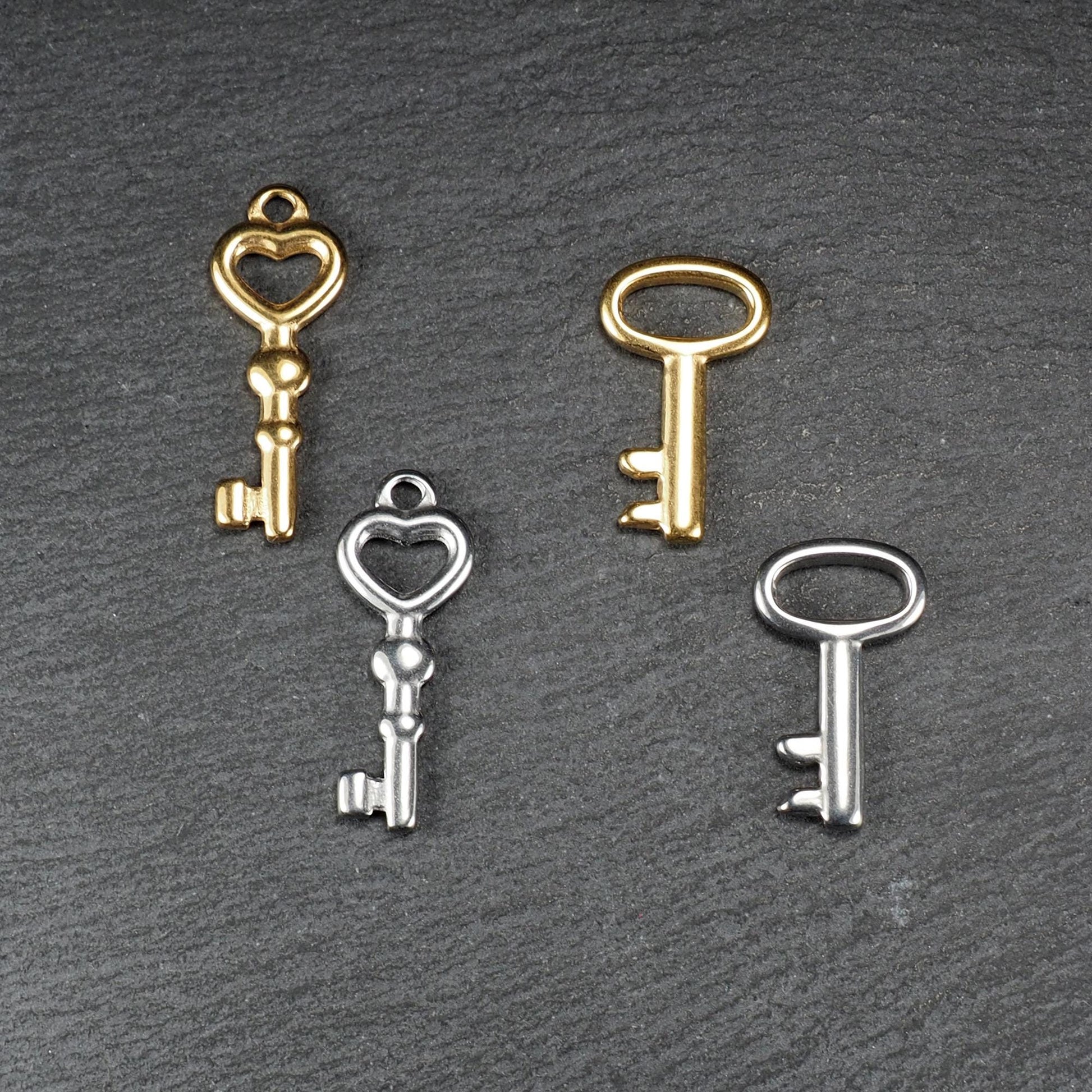 Vier glänzende Schlüsselanhänger, zwei vergoldet und zwei silberfarben; zwei mit herzförmiger Öse, zwei mit ovaler Öse.