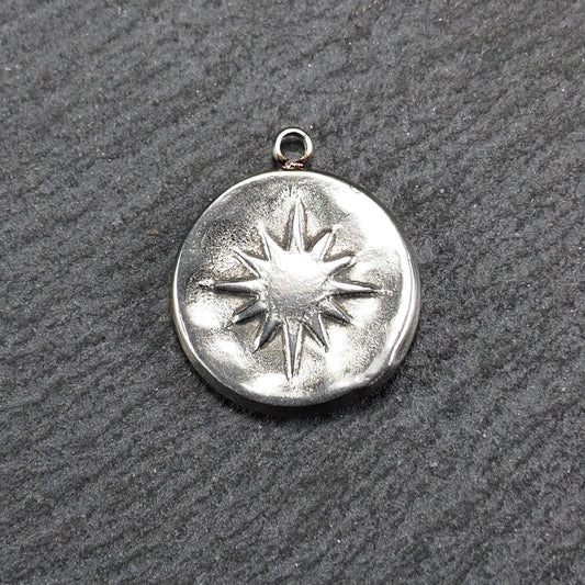 Runder silberfarbener Metallanhänger mit leicht strukturierter, glänzender Oberfläche, reliefierter Achtstrahlsonne und kleiner Aufhängeöse oben.