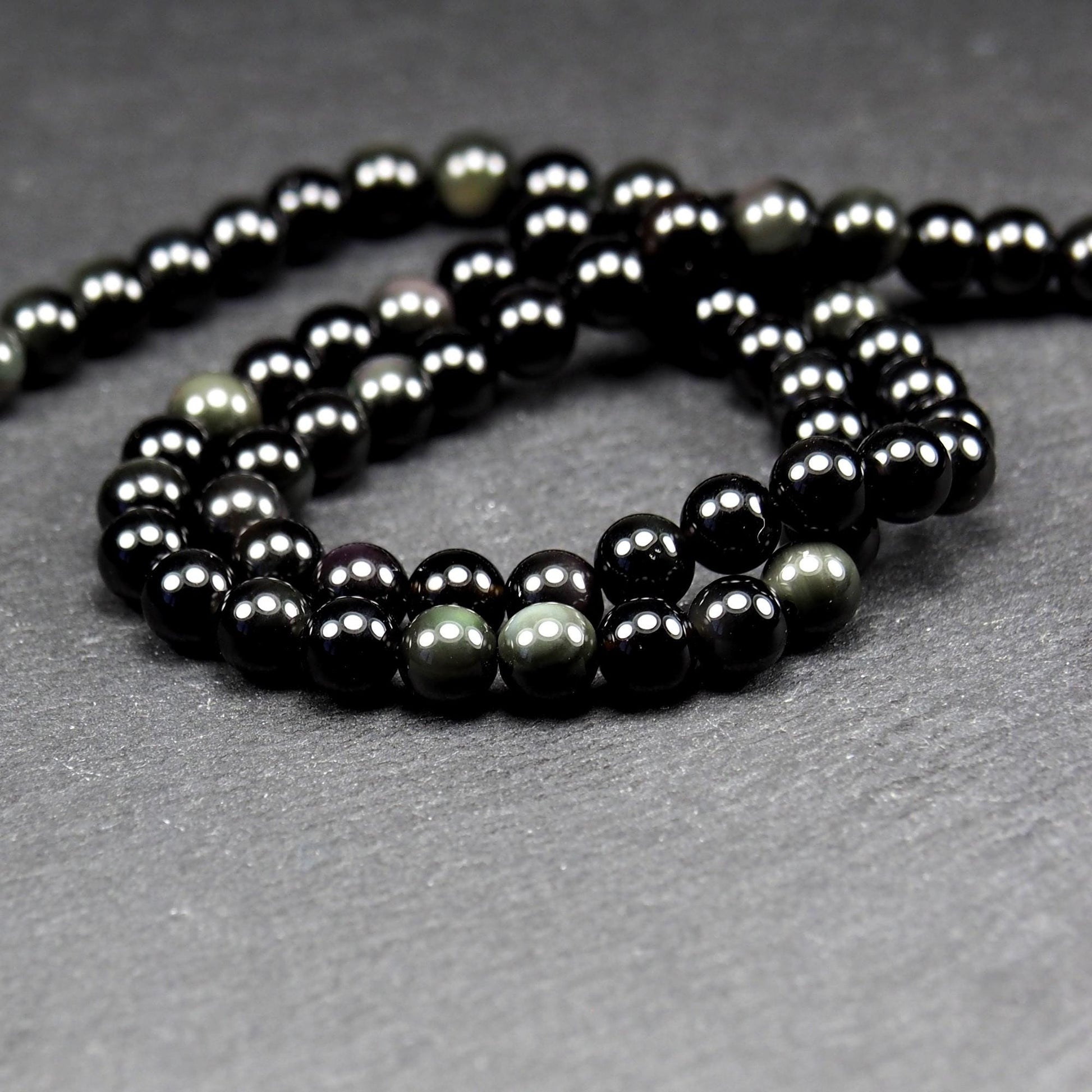 Aufgereihter Perlenstrang aus tiefschwarzen, hochglänzend-polierten, kugelförmigen Obsidianperlen mit glatter Oberfläche.