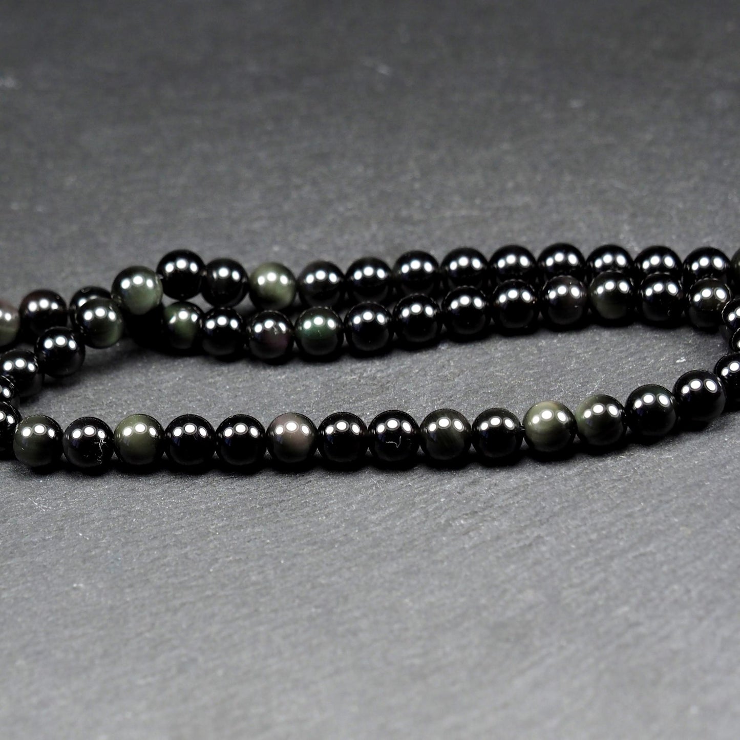 Aufgereihter Perlenstrang aus tiefschwarzen, hochglänzend-polierten, kugelförmigen Obsidianperlen mit glatter Oberfläche.