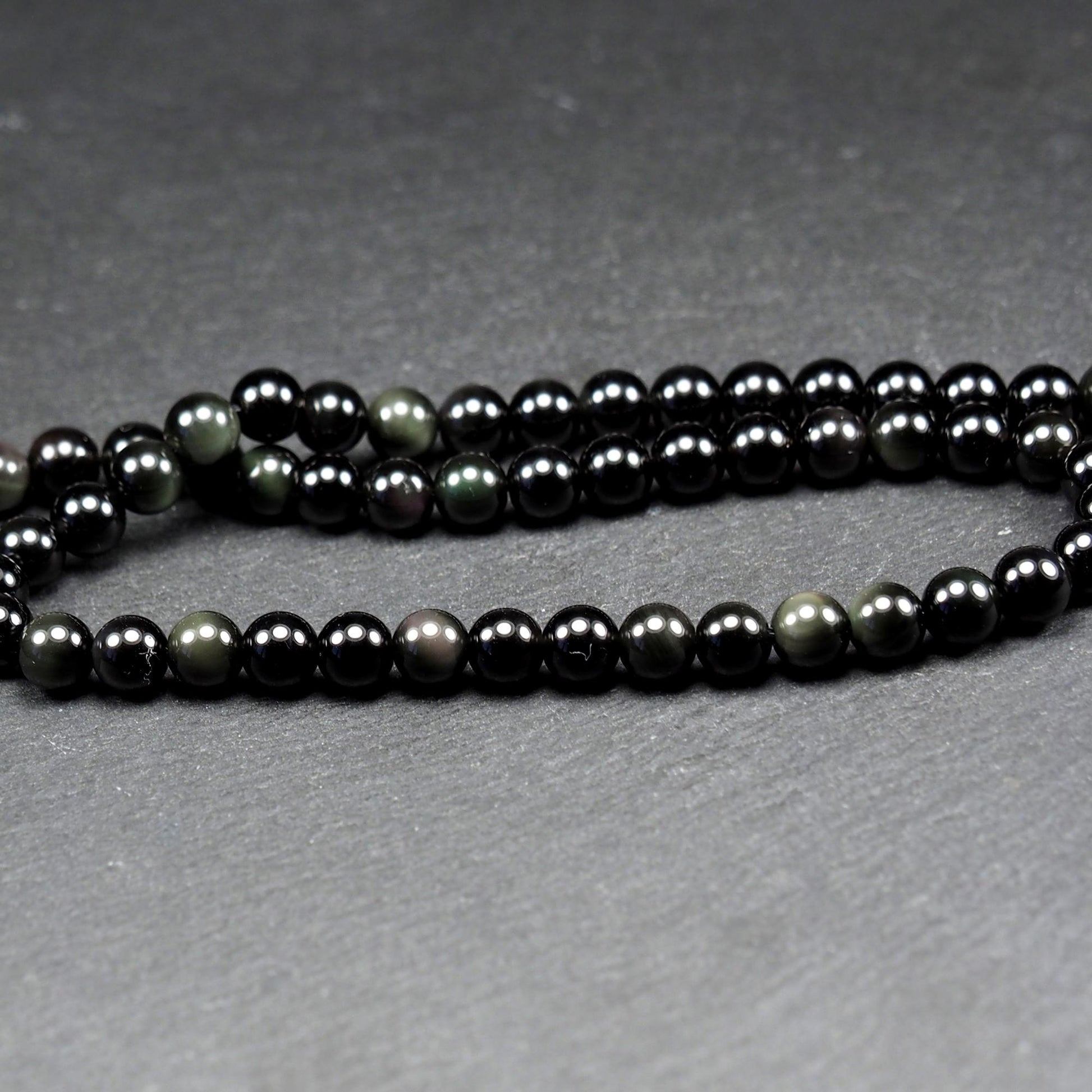 Aufgereihter Perlenstrang aus tiefschwarzen, hochglänzend-polierten, kugelförmigen Obsidianperlen mit glatter Oberfläche.