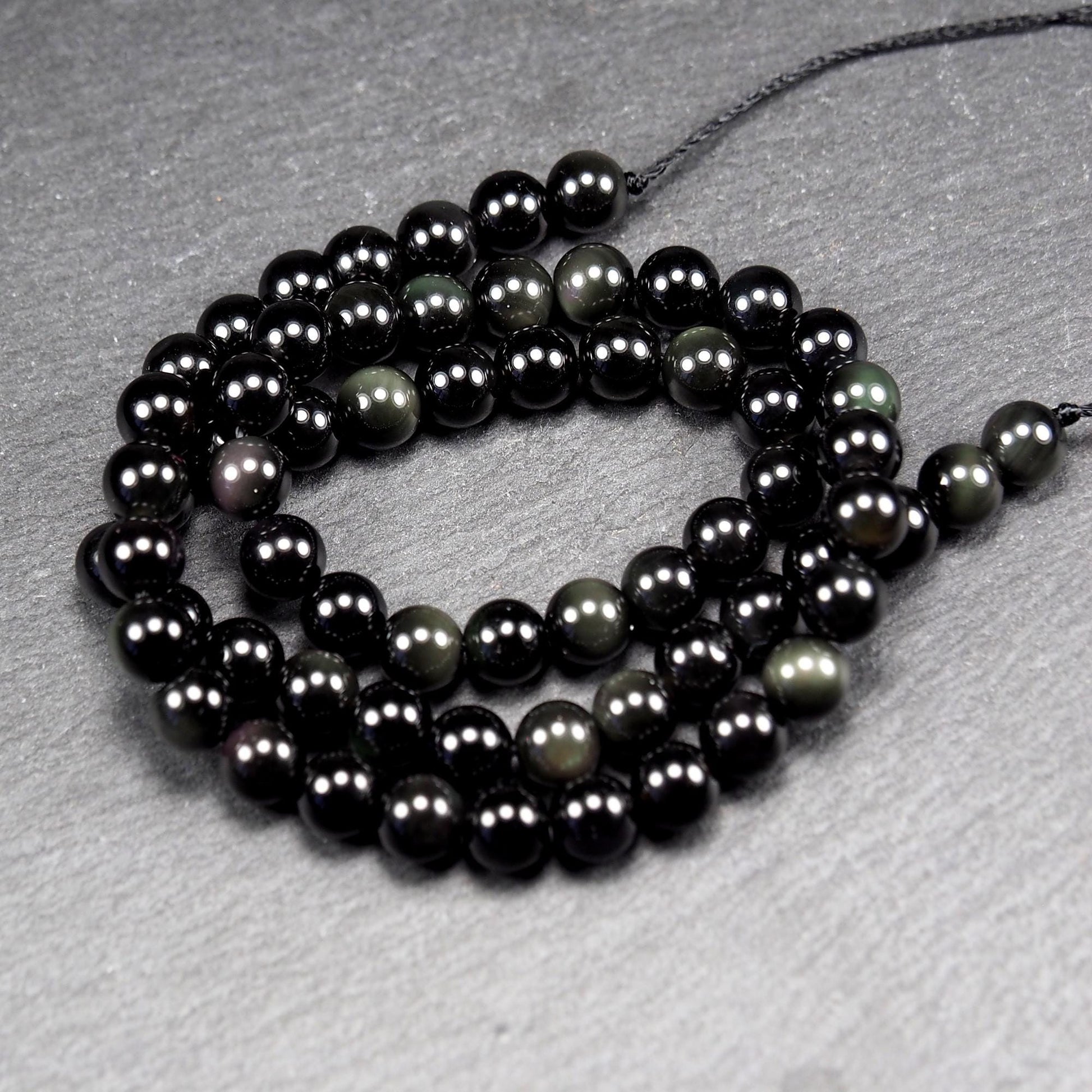 Aufgereihter Perlenstrang aus tiefschwarzen, hochglänzend-polierten, kugelförmigen Obsidianperlen mit glatter Oberfläche.