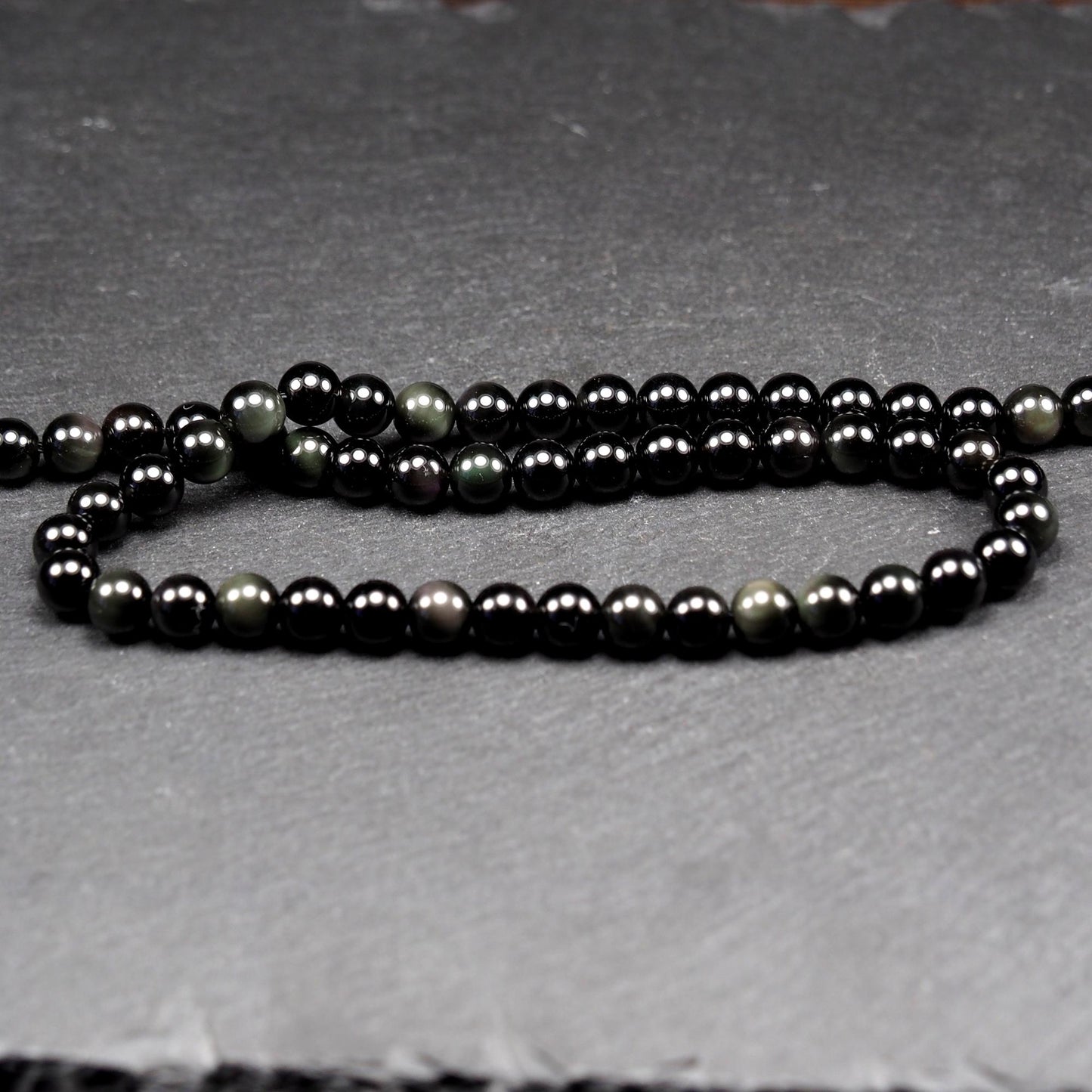 Aufgereihter Perlenstrang aus tiefschwarzen, hochglänzend-polierten, kugelförmigen Obsidianperlen mit glatter Oberfläche.