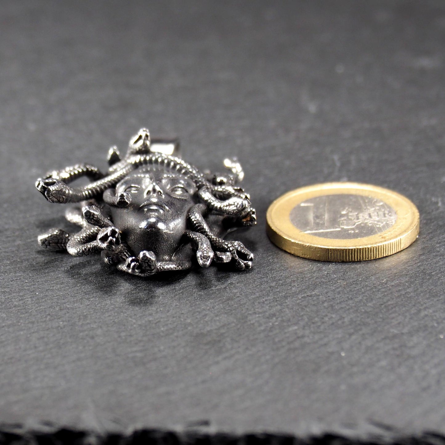 Silberfarbener, dreidimensionaler und glänzender Medusa-Anhänger in Relief mit menschlichem Gesicht und vielen schlangenförmigen Haaren, sichtbarer Öse.