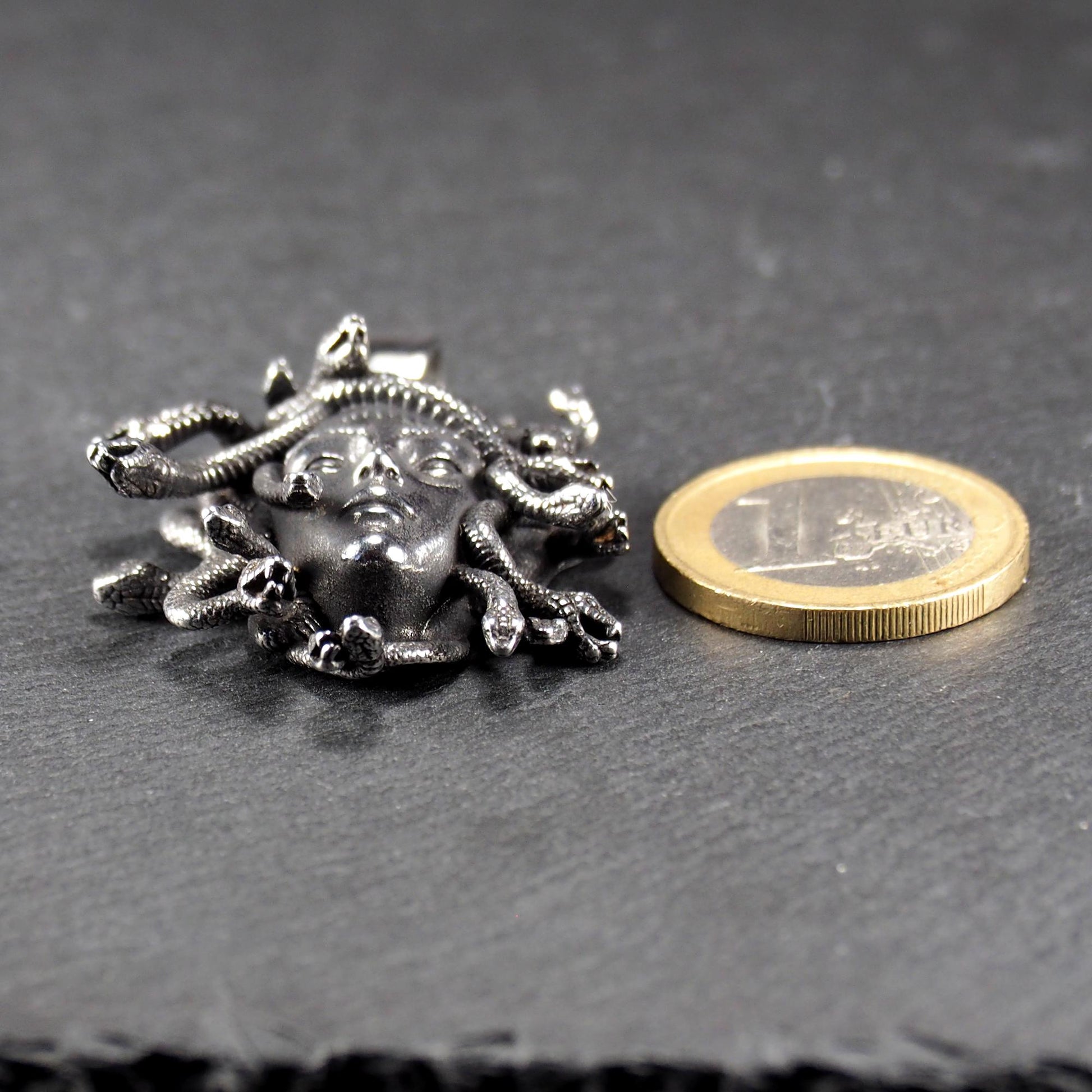 Silberfarbener, dreidimensionaler und glänzender Medusa-Anhänger in Relief mit menschlichem Gesicht und vielen schlangenförmigen Haaren, sichtbarer Öse.