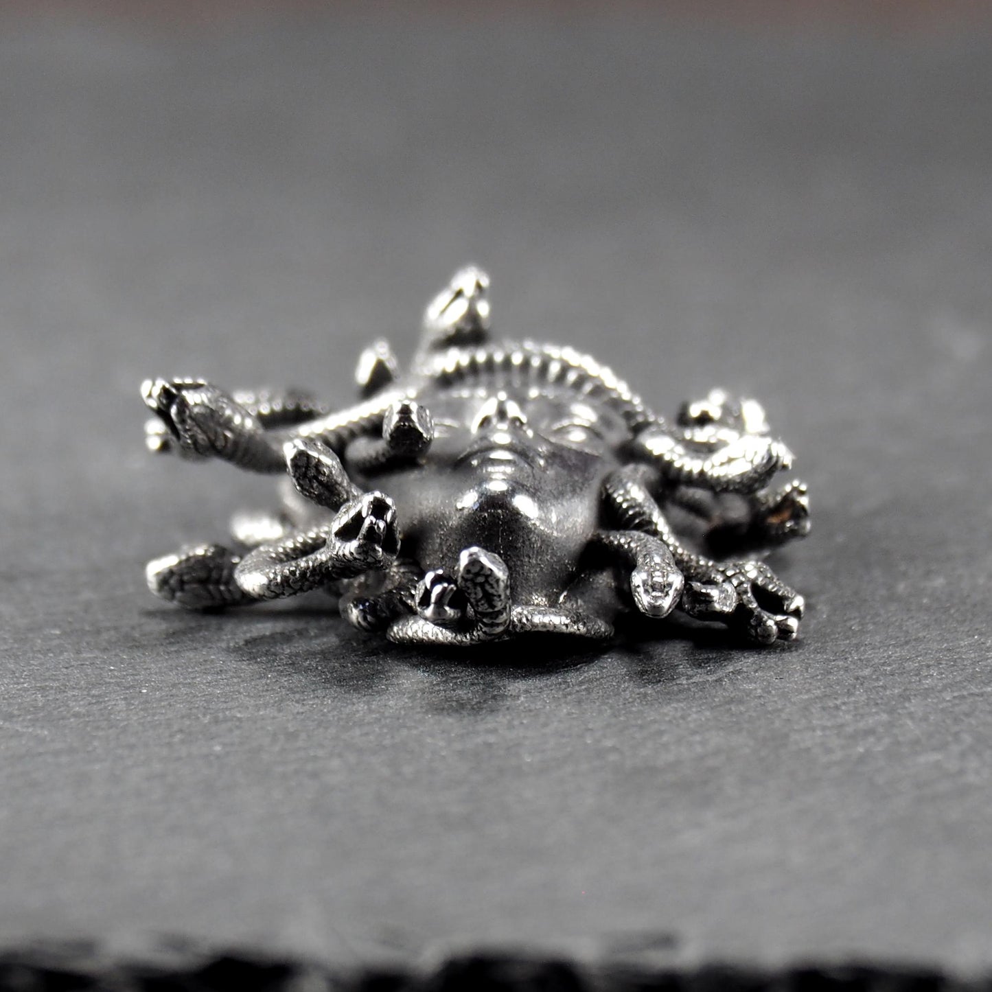 Silberfarbener, dreidimensionaler und glänzender Medusa-Anhänger in Relief mit menschlichem Gesicht und vielen schlangenförmigen Haaren, sichtbarer Öse.