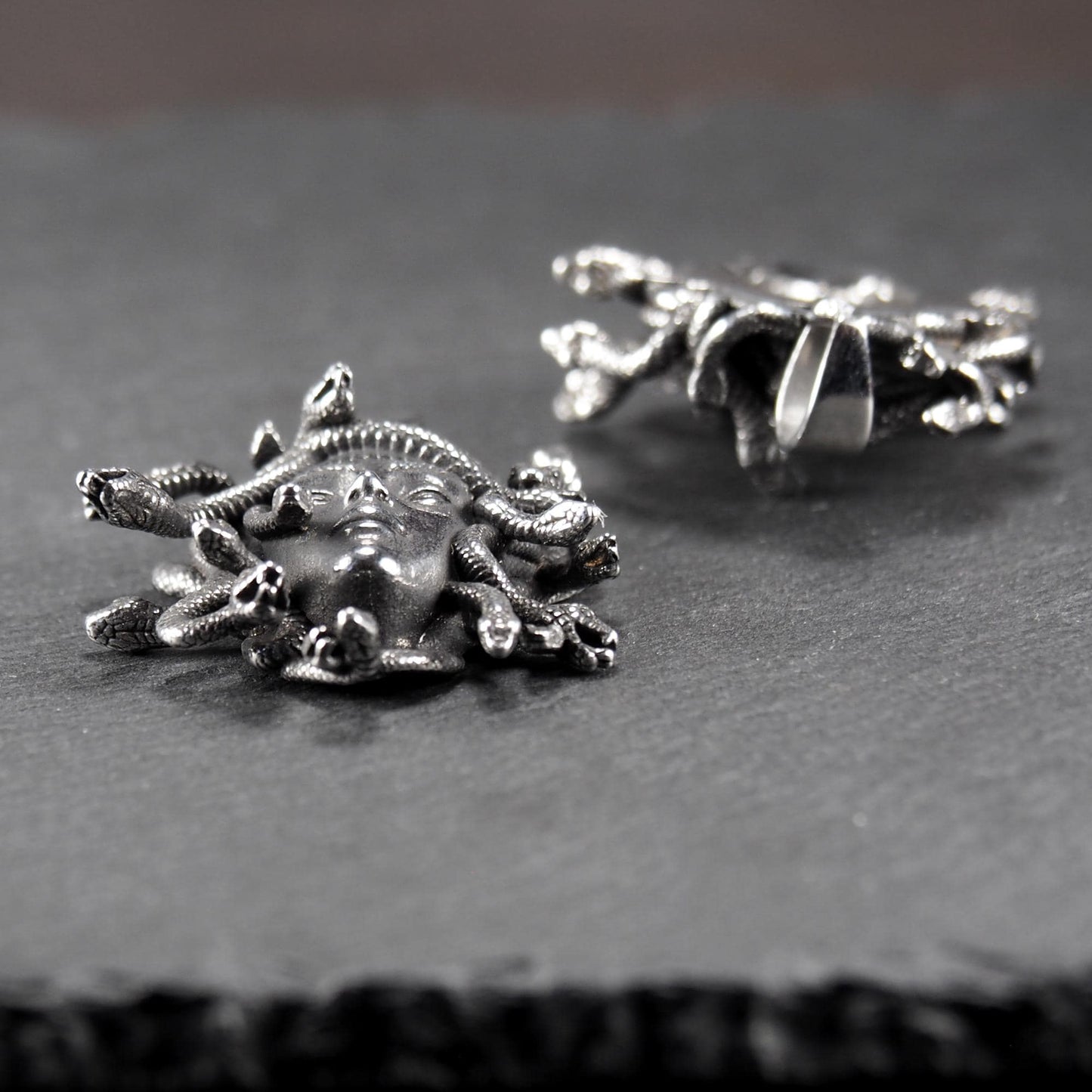 Silberfarbener, dreidimensionaler und glänzender Medusa-Anhänger in Relief mit menschlichem Gesicht und vielen schlangenförmigen Haaren, sichtbarer Öse.