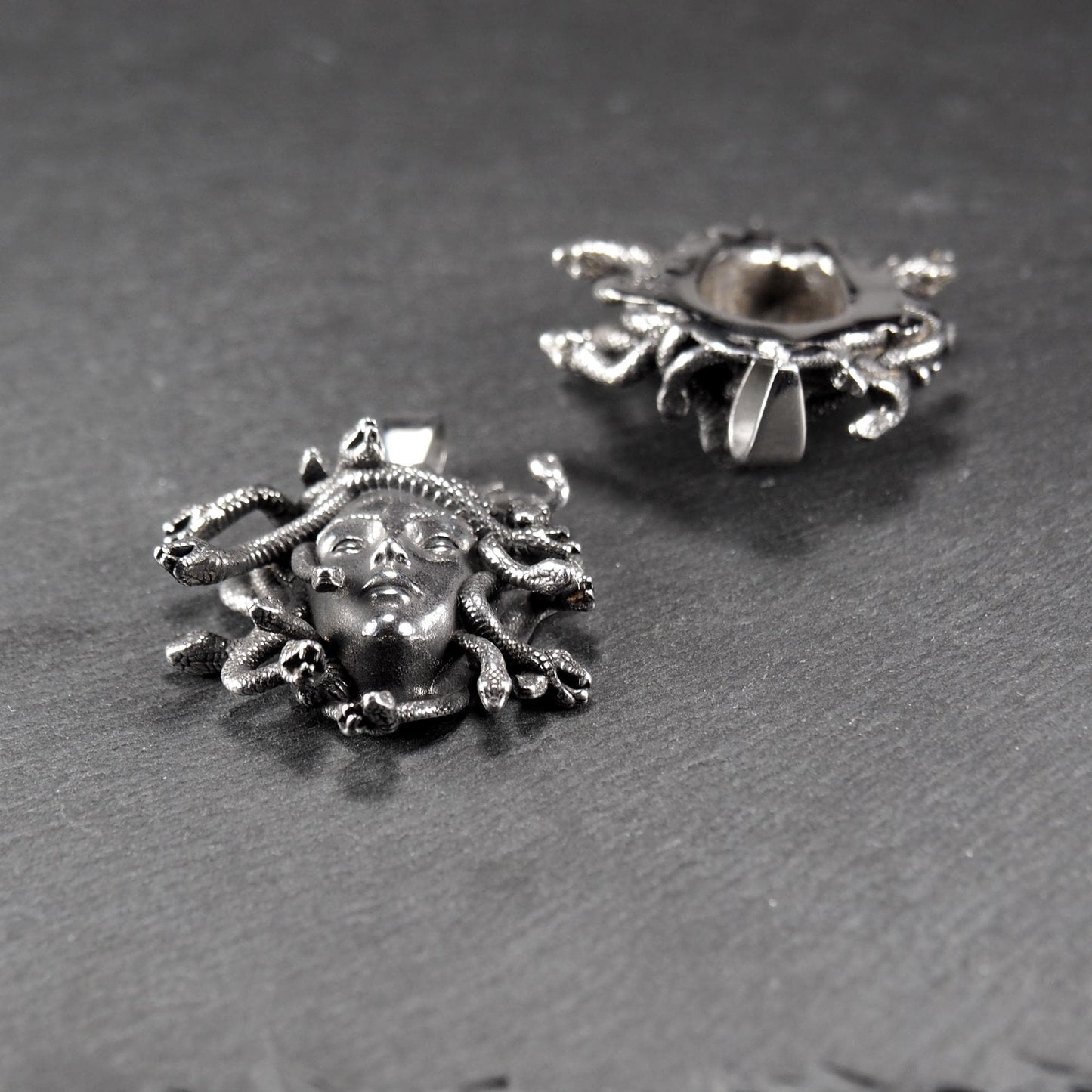 Silberfarbener, dreidimensionaler und glänzender Medusa-Anhänger in Relief mit menschlichem Gesicht und vielen schlangenförmigen Haaren, sichtbarer Öse.