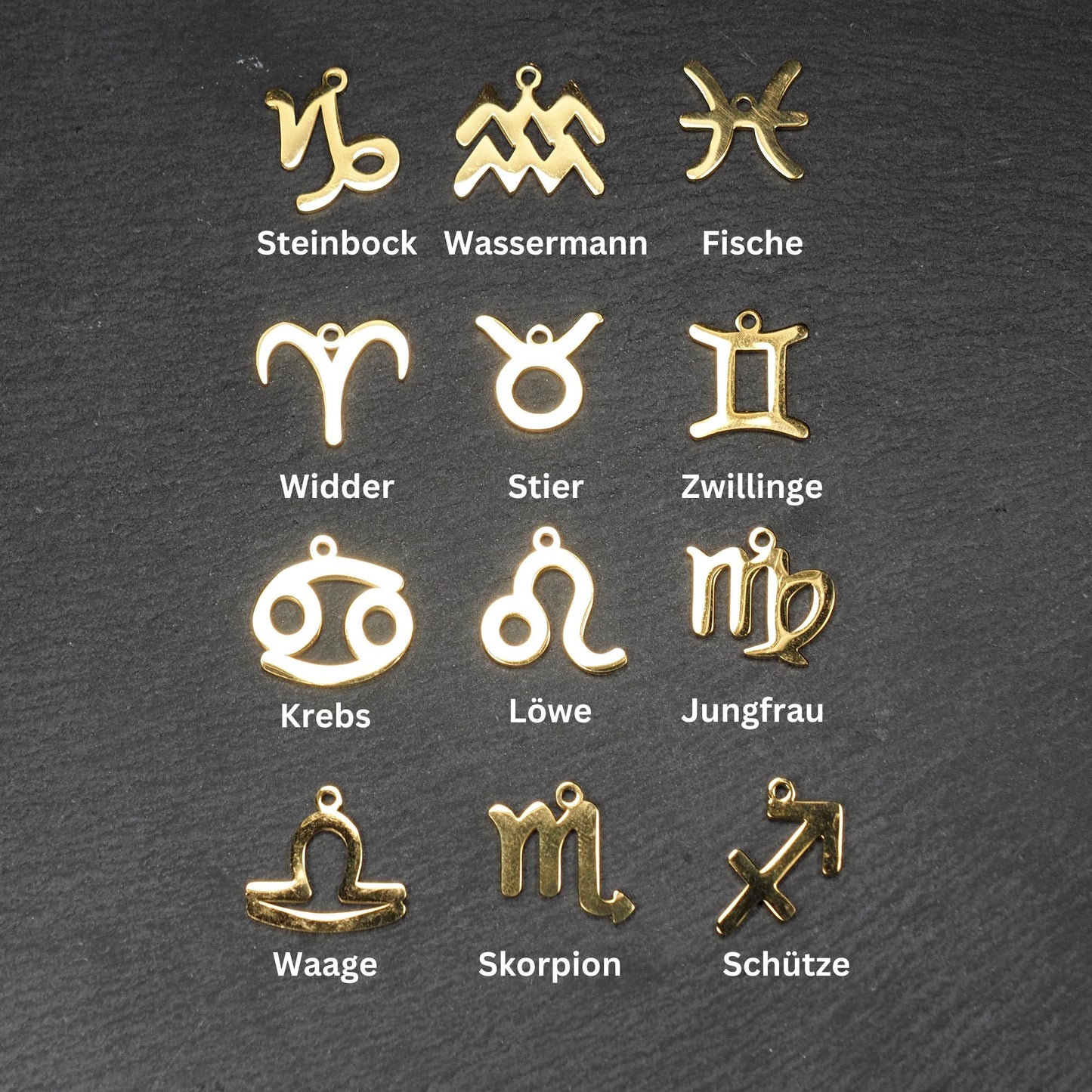 Zwölf flache, vergoldete Sternzeichen-Anhänger aus Metall mit minimalistischer, durchbrochener Kontur und integrierter Öse auf dunklem Hintergrund.