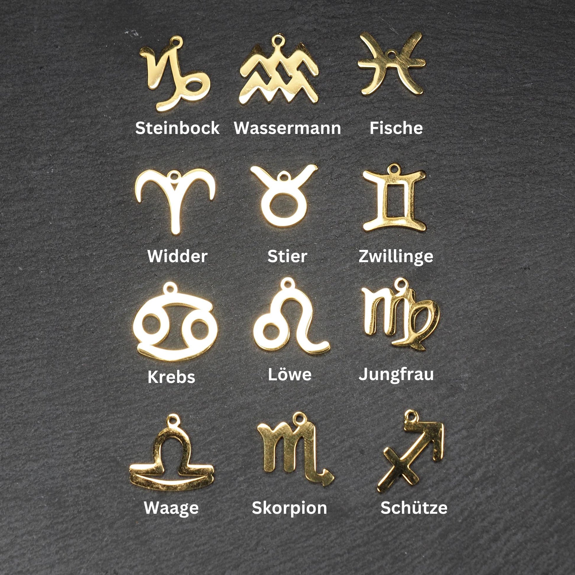 Zwölf flache, vergoldete Sternzeichen-Anhänger aus Metall mit minimalistischer, durchbrochener Kontur und integrierter Öse auf dunklem Hintergrund.